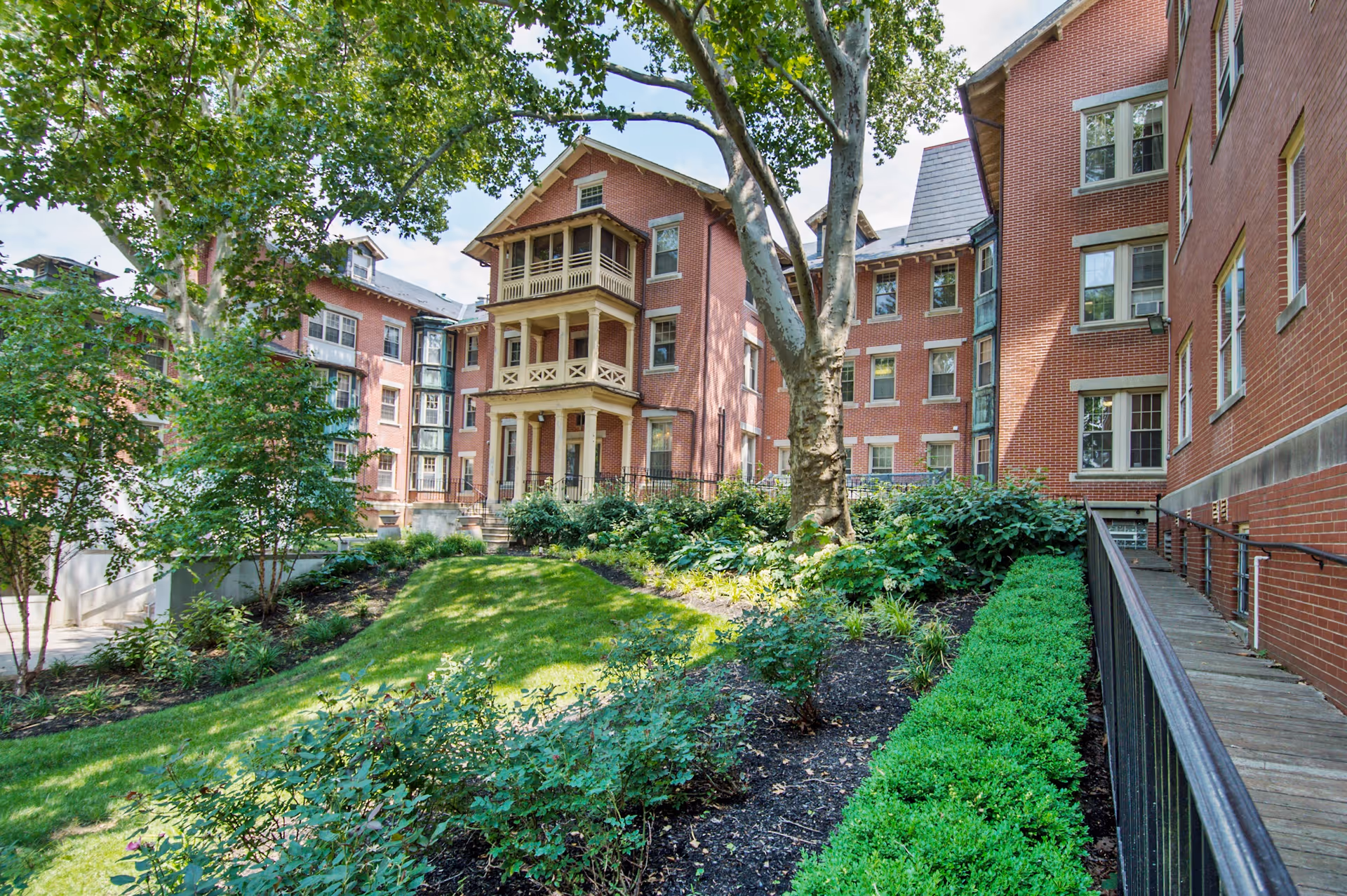 Brick senior living buildings enclose a landscaped courtyard with mature trees and shrubs.