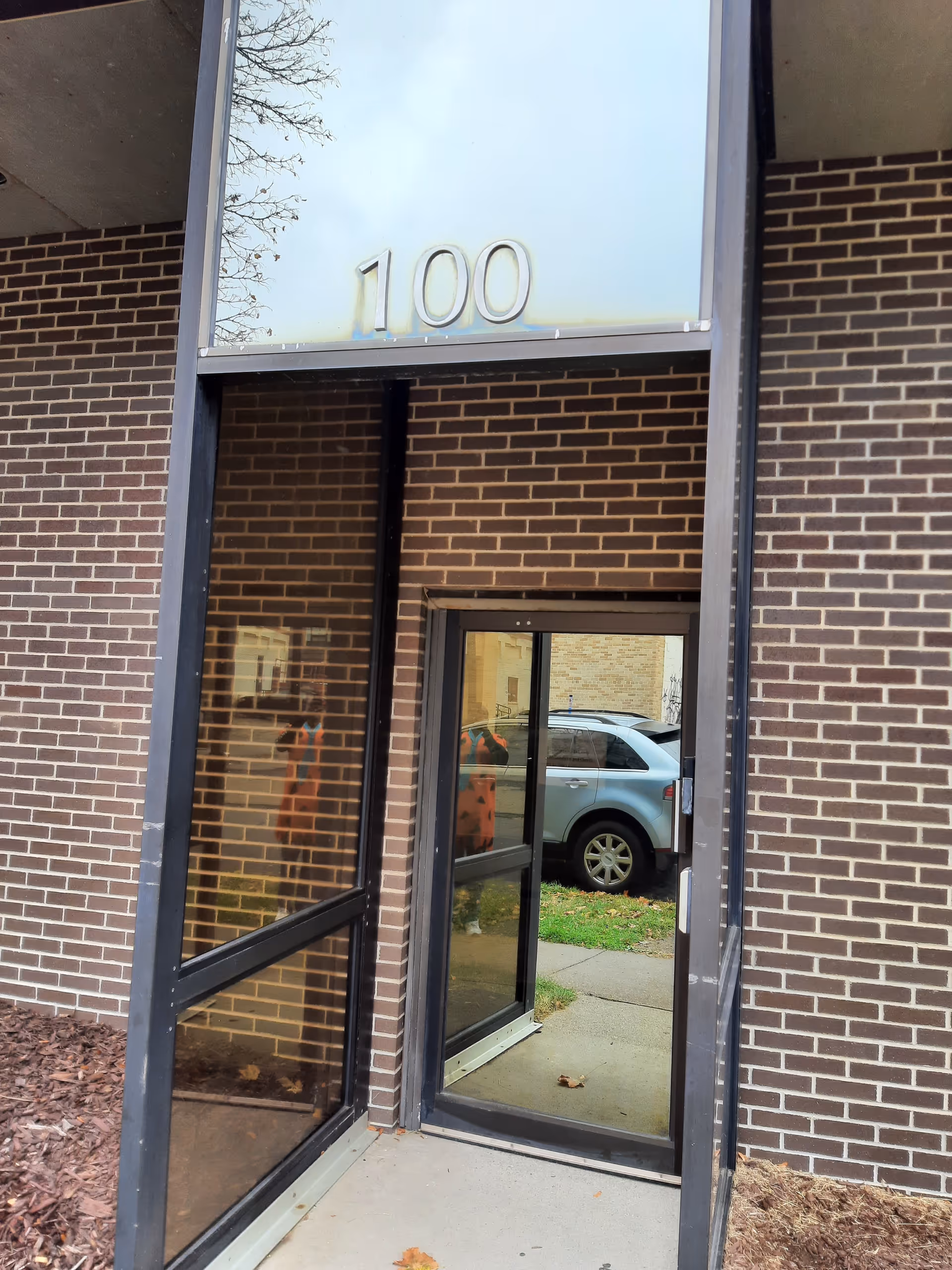 Exterior brick entrance with glass doors and the number 100 above the doorway.