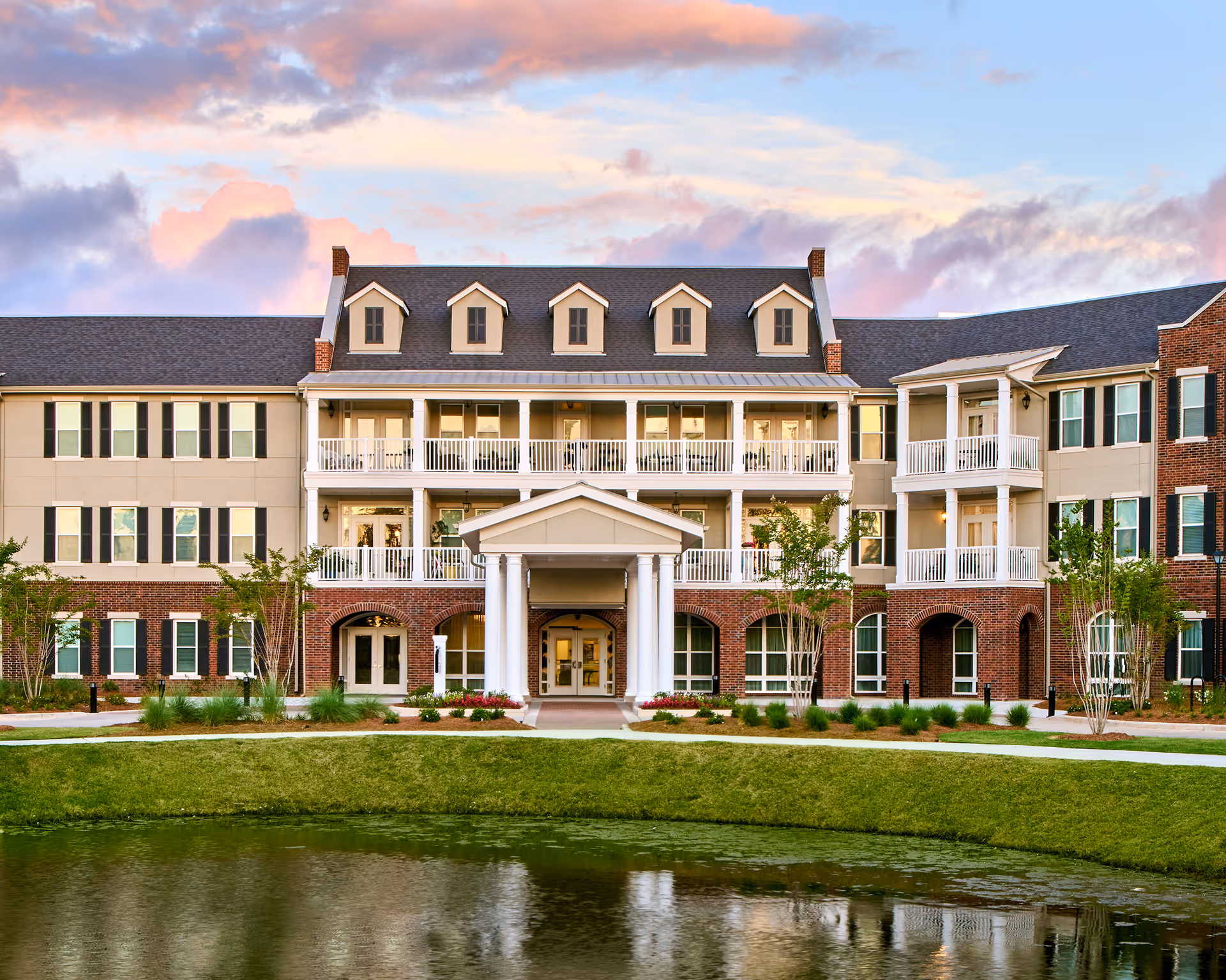 Front exterior view of The Glen Retirement System building with a pond and landscaped greenery in the foreground under a colorful sky at sunset.