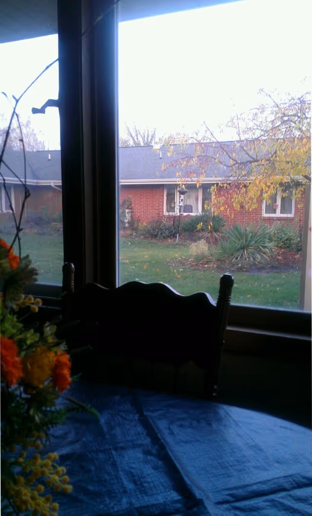 Indoor dining area with a blue tablecloth, flowers, and a window view outside.