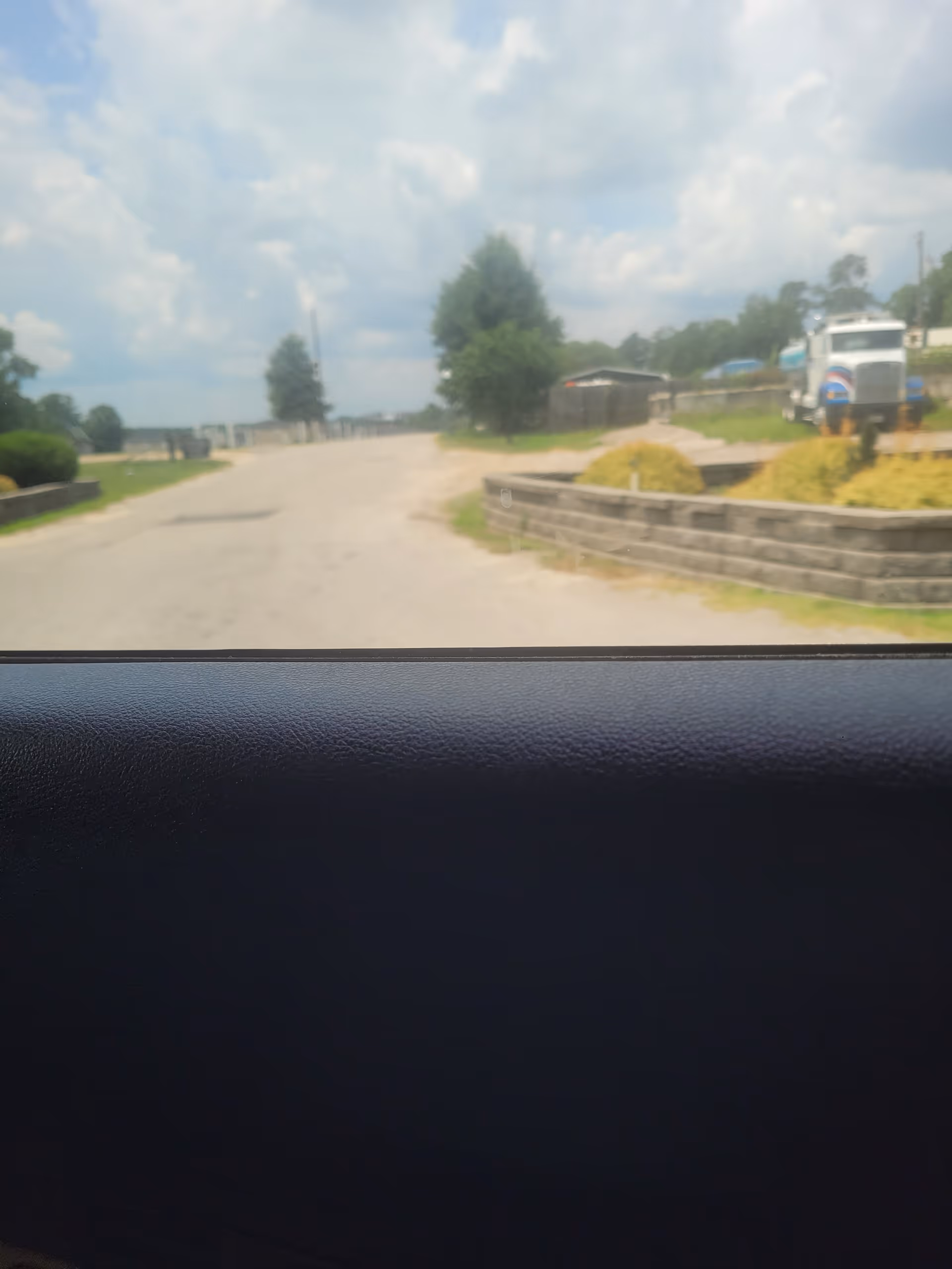 View from inside a vehicle looking out at a road, truck, and landscaped greenery.