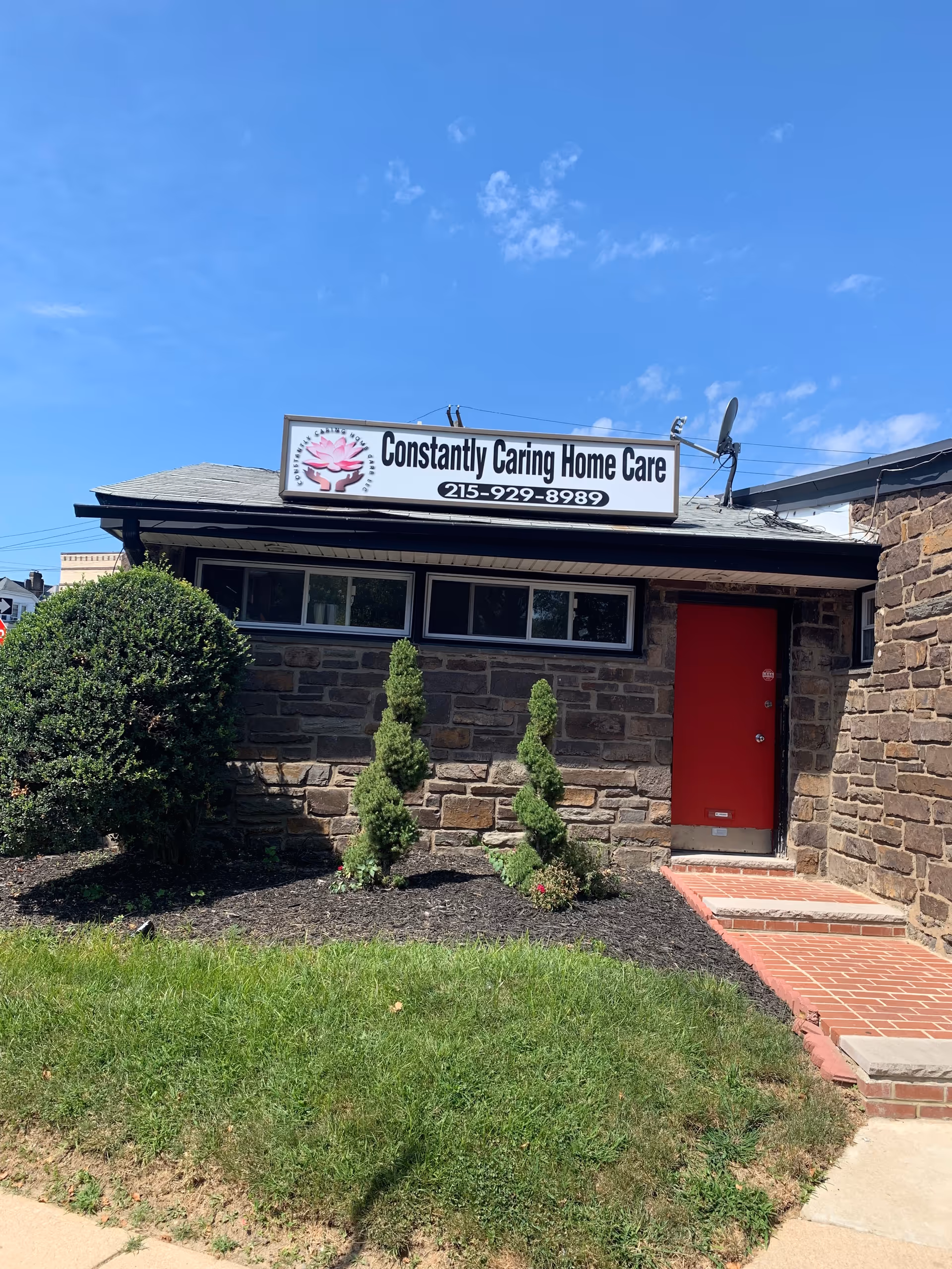 Front exterior of Constantly Caring Home Care building with a red door and sign.