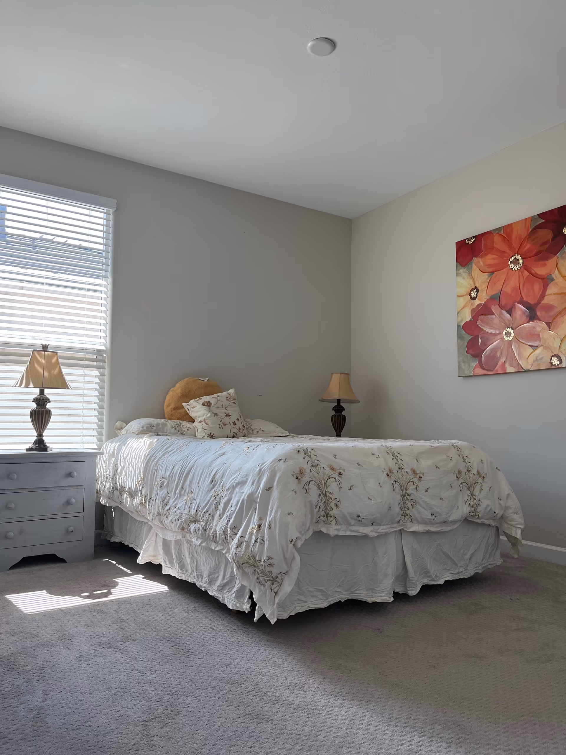 A tidy bedroom with a bed, nightstands, lamps, and floral wall art.