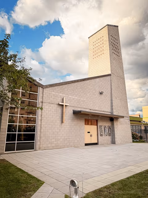 Exterior view of a modern church with a cross and tall tower.