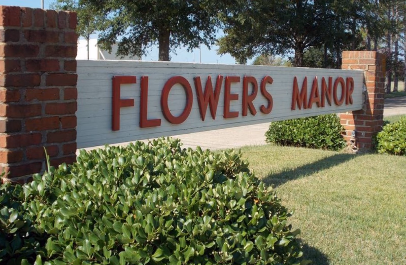 Entrance sign for Flowers Manor with brick pillars and manicured shrubs.