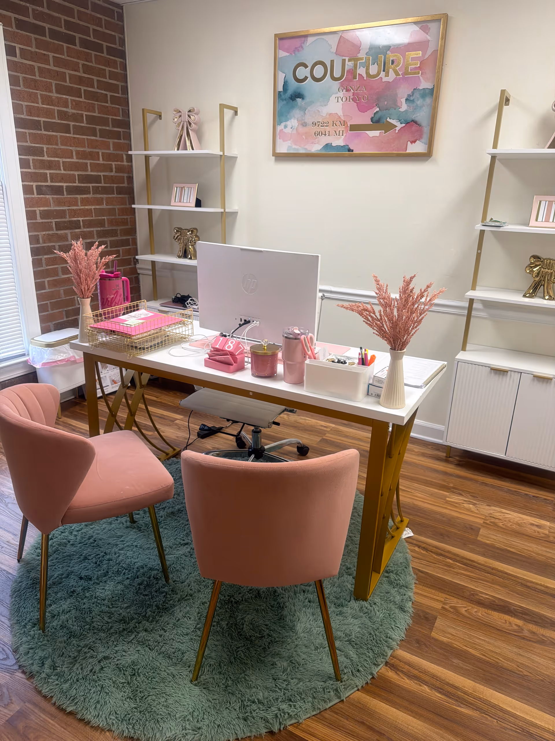 Pink-chic office desk setup with computer, pink chairs, and pastel decor.