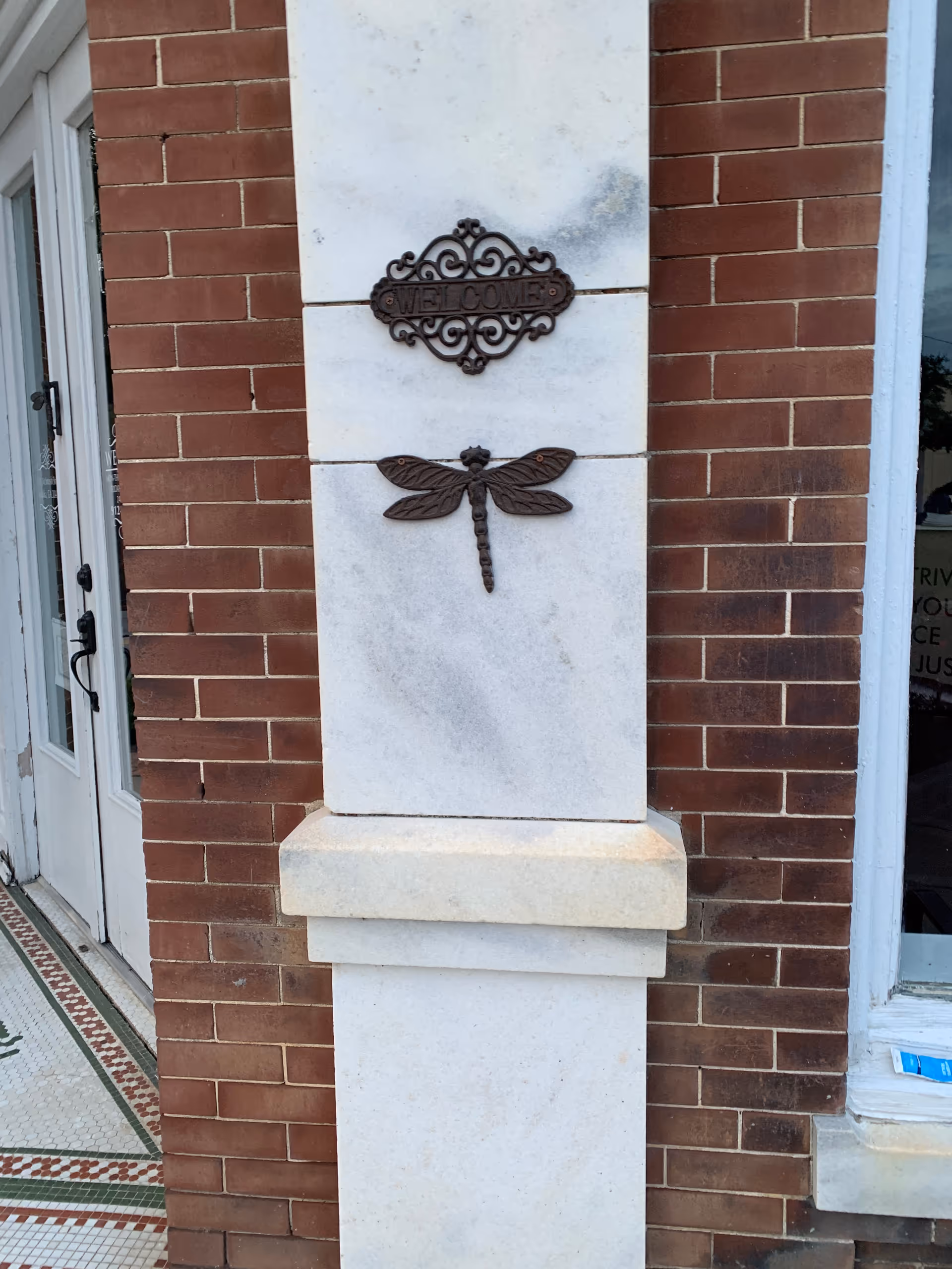 Brick exterior with a white stone column, welcome sign, and dragonfly plaque at the entrance.