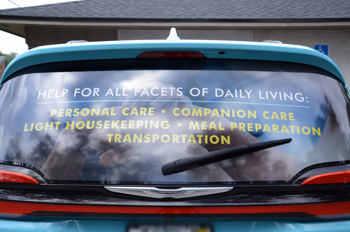 Rear of teal car with large home care services advertisement on rear window