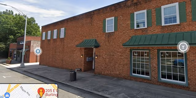 Brick building with green awnings and large showroom-style windows along a sidewalk.