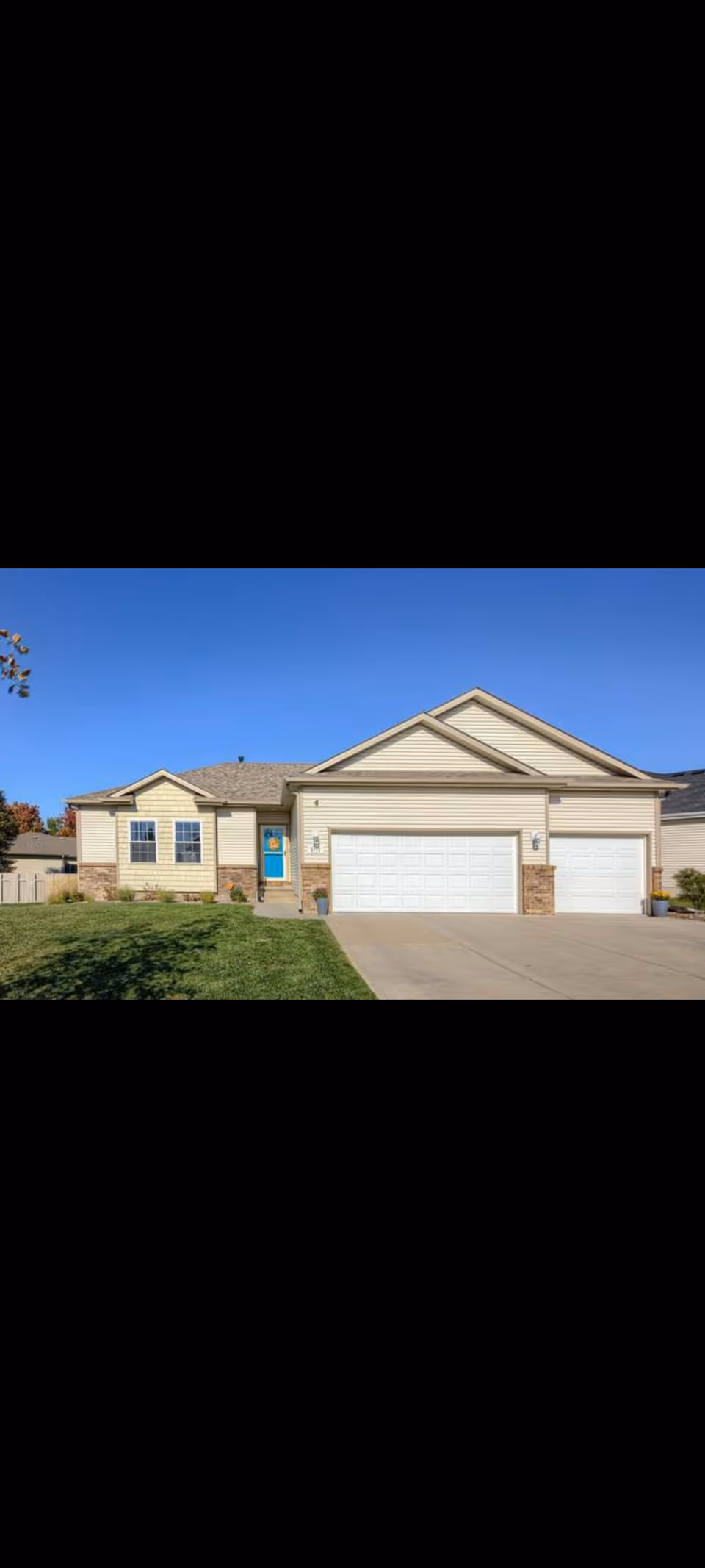 Front view of a beige suburban house with a two car garage and green lawn.