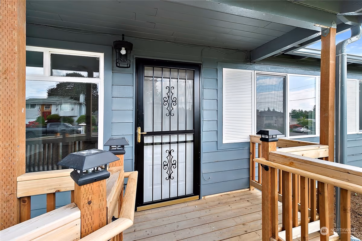 Front porch of a blue home with a black security door and wooden railing.