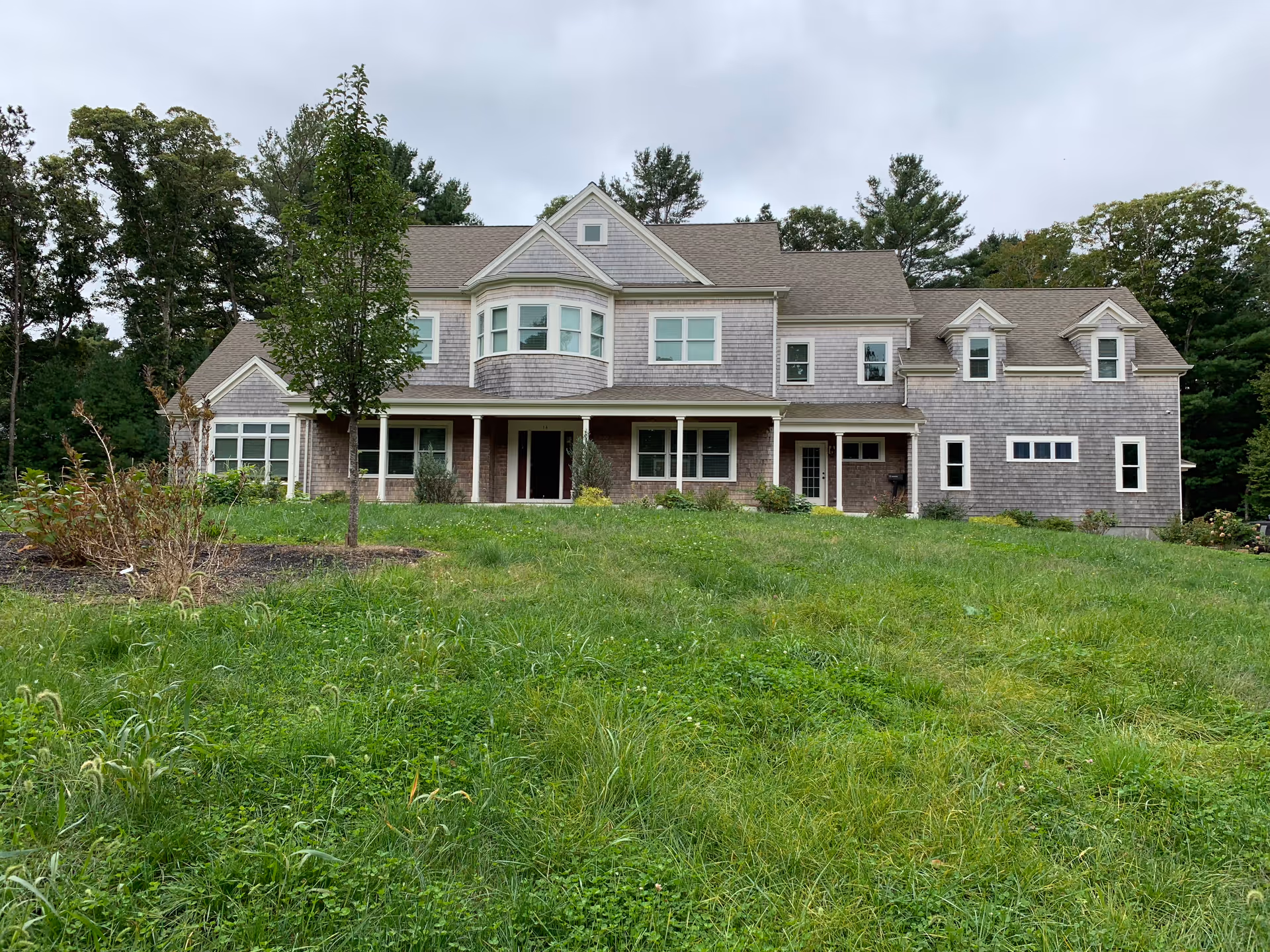 A large house-like senior living facility with a front lawn and trees near a cloudy sky.