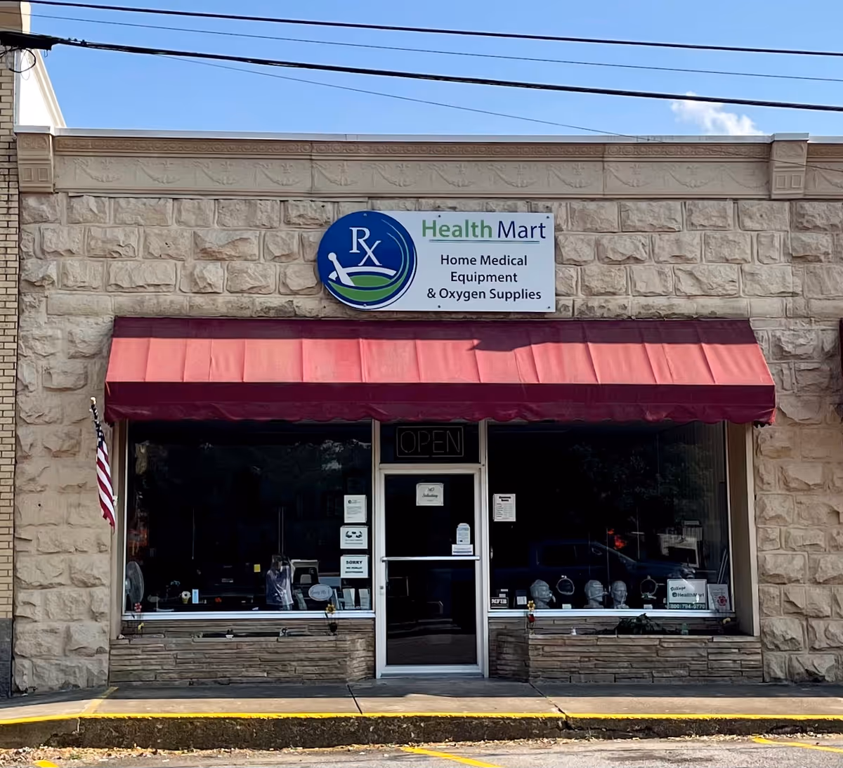 Stone facade storefront with Health Mart sign, red awning, glass entrance, and American flag.
