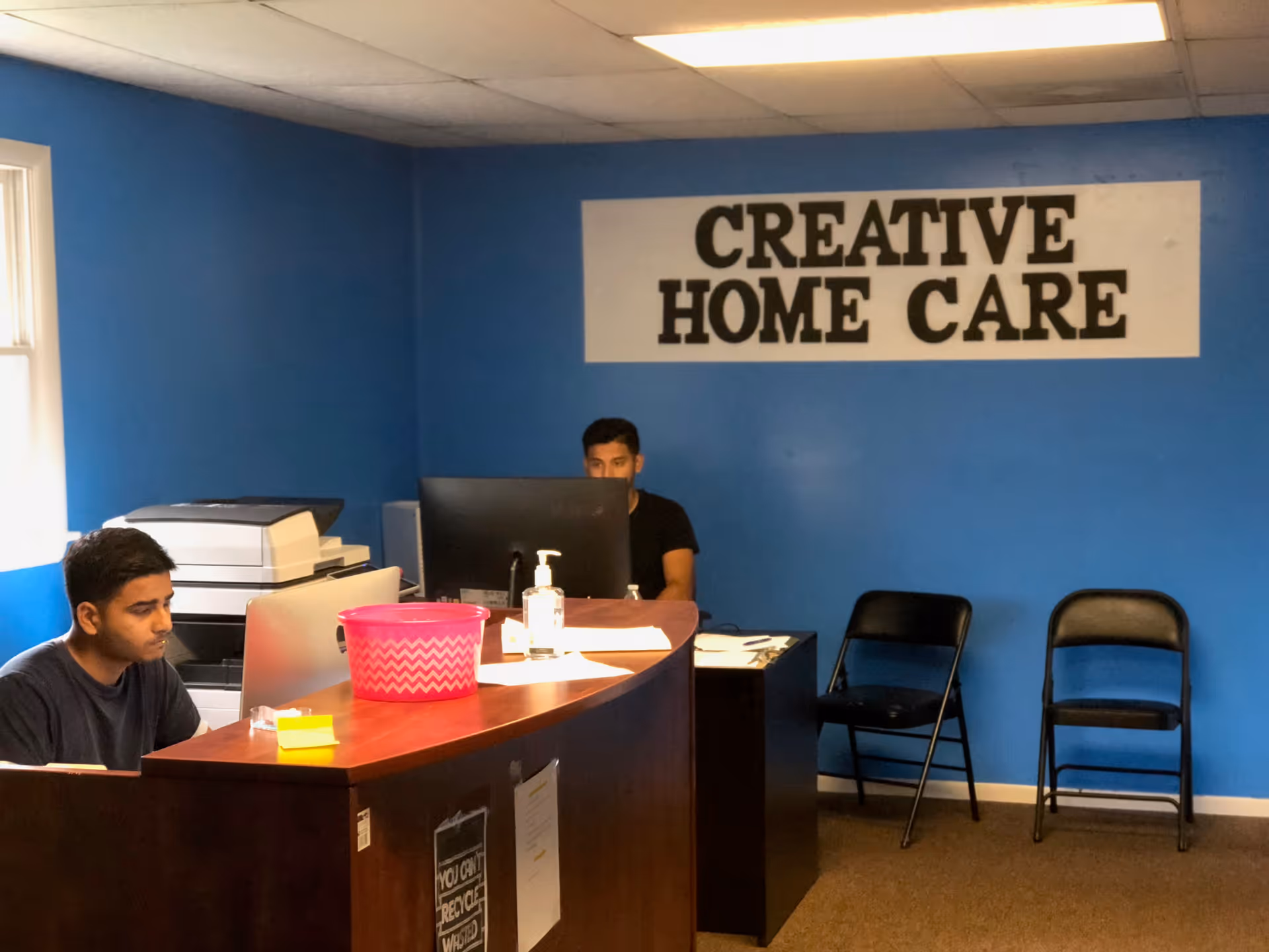 Reception area with two staff at a curved desk under a Creative Home Care sign.
