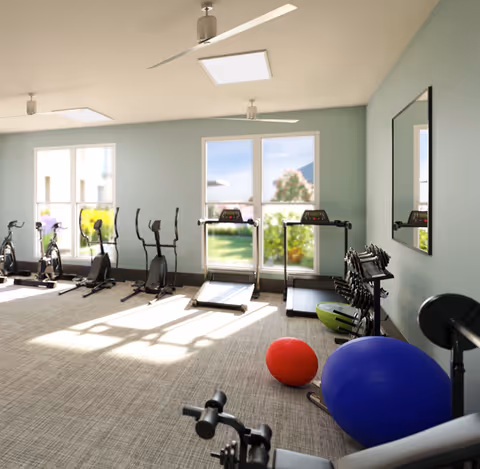 A bright indoor fitness room with treadmills, bikes, weights, and exercise balls.