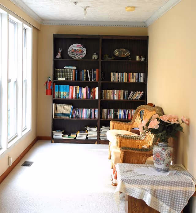 Bright interior reading nook with a tall bookshelf, wicker chairs, and a floral vase.