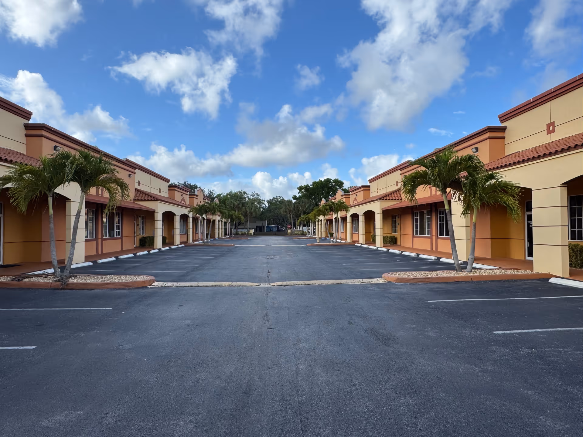Clear blue sky above a parking lot flanked by connected senior living buildings with palm trees.
