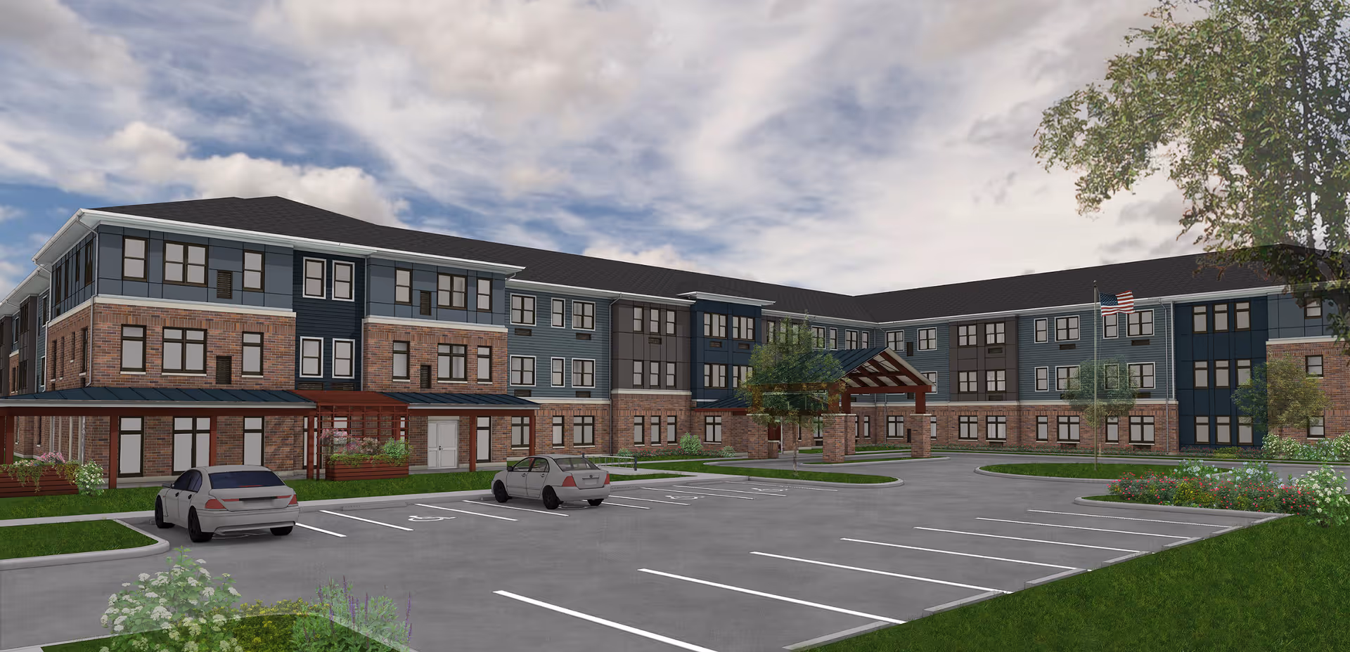 Exterior view of a three-story senior living facility building with a combination of brick and blue siding. The building has numerous windows and a covered entrance. There is a parking lot in front with a few cars parked, landscaped greenery, and an American flag flying near the entrance under a partly cloudy sky.