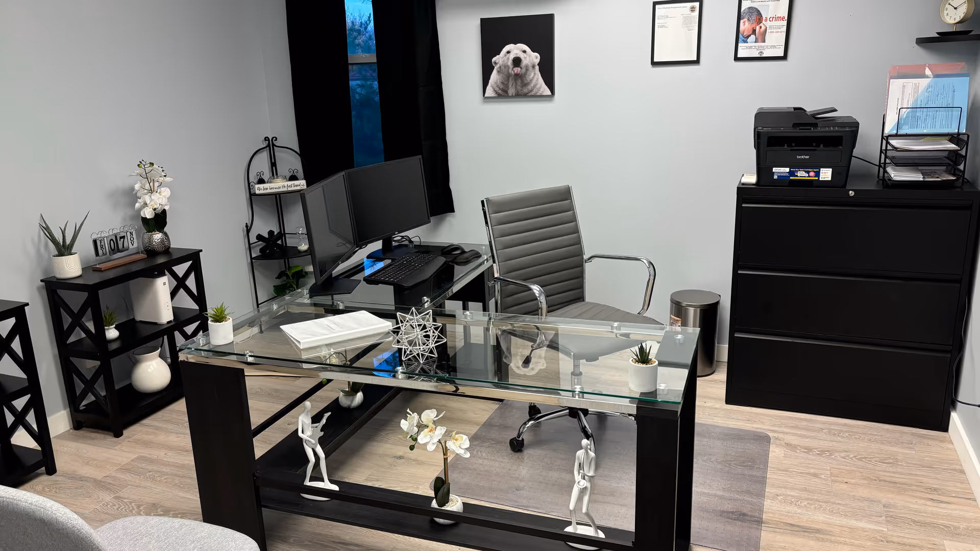 A glass desk with computer setup, modern office chair, and filing cabinet in a small office.