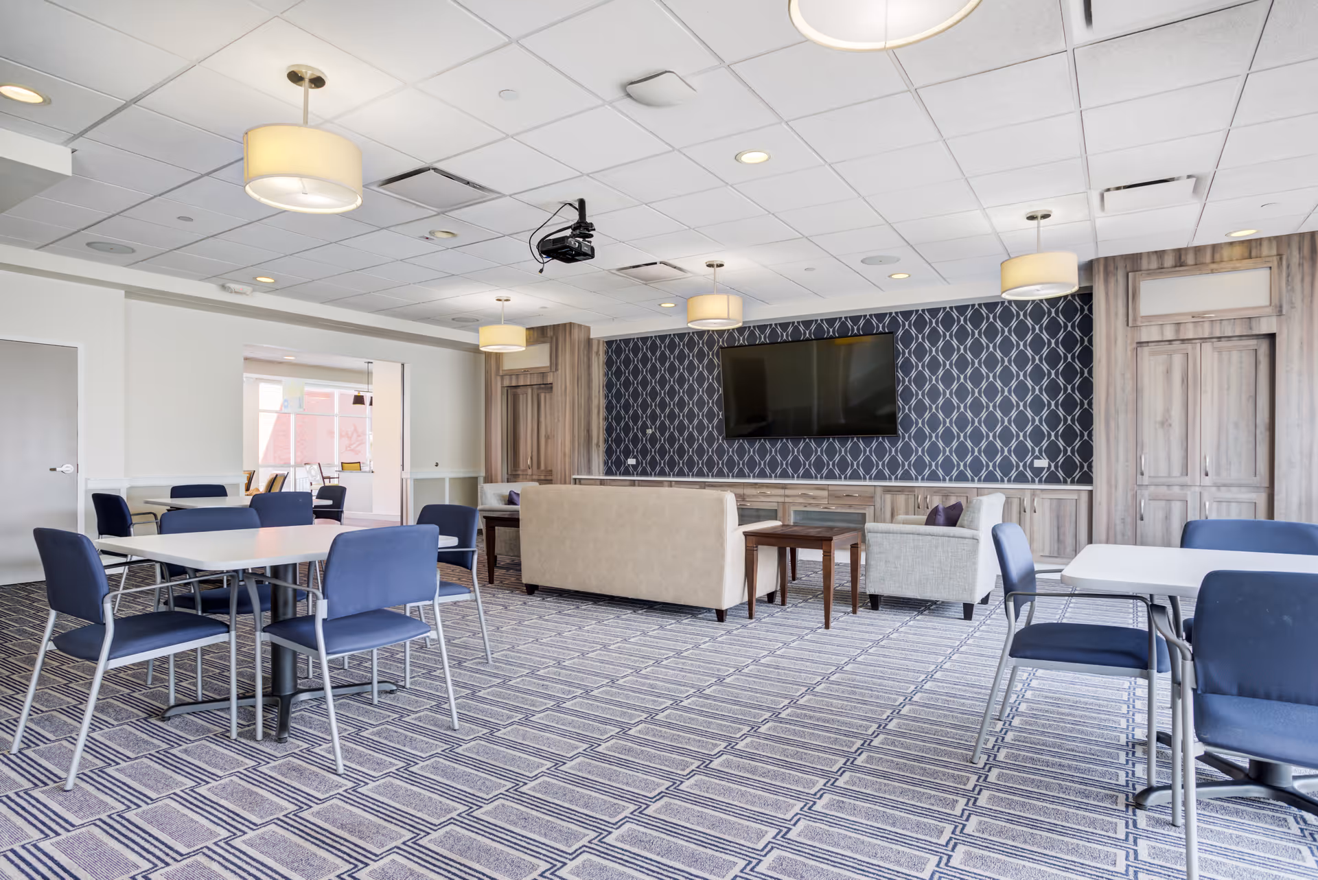 Senior living common area with blue chairs, tables, sofas, and a wall-mounted TV