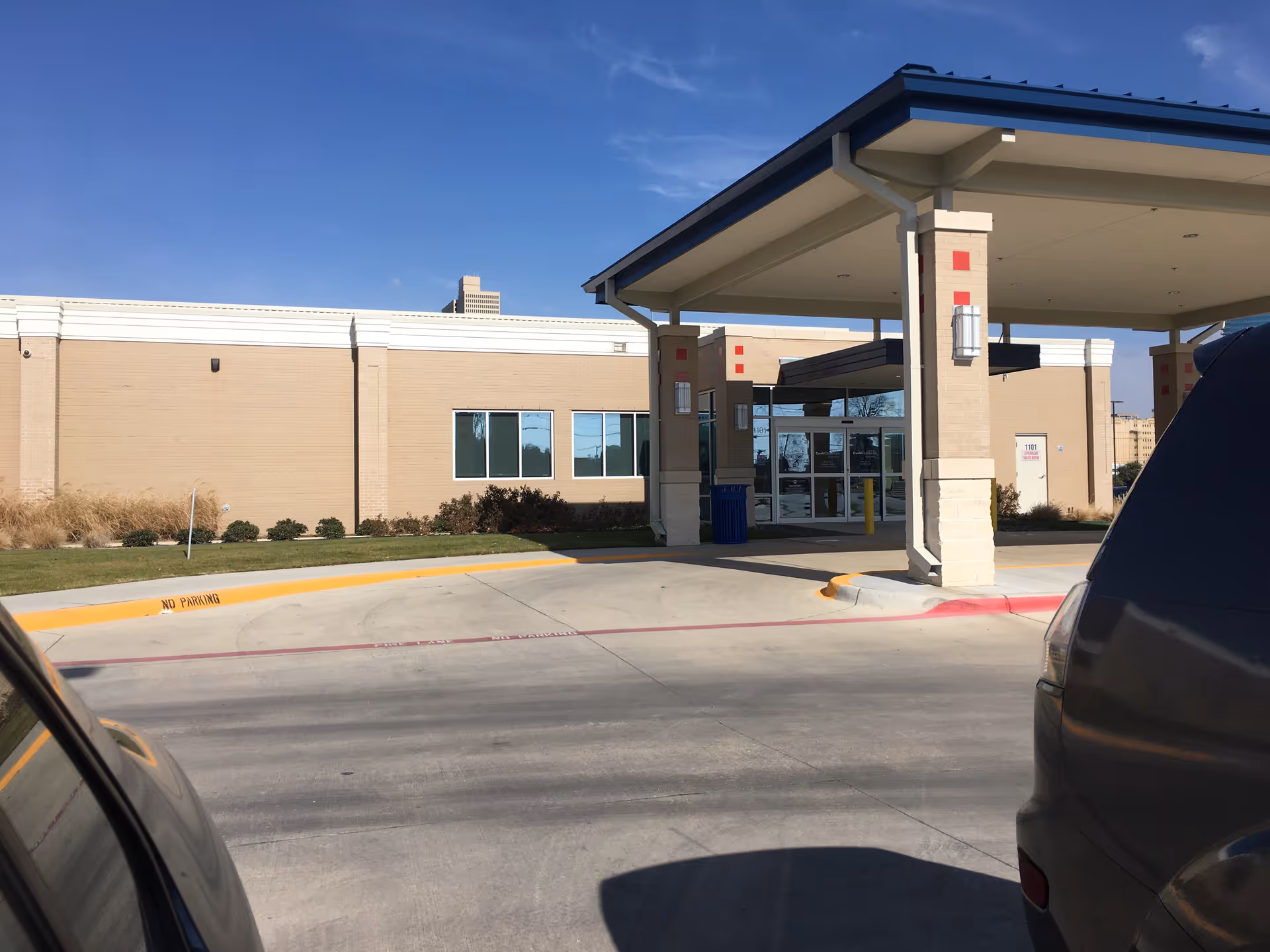 Front exterior view of a single-story medical facility with a covered entrance and parked cars.