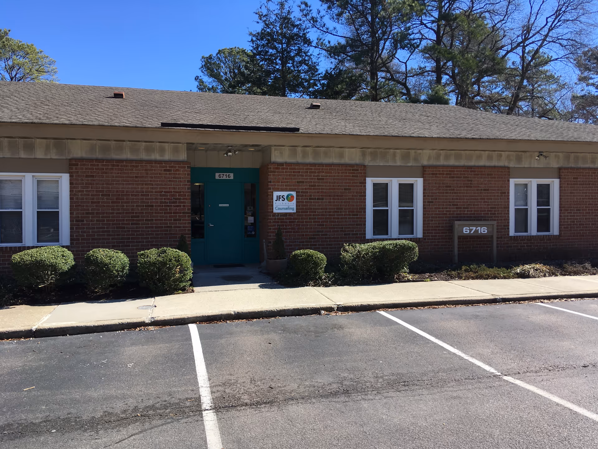 Brick building with teal front entrance, signage, and trimmed bushes along the walkway.