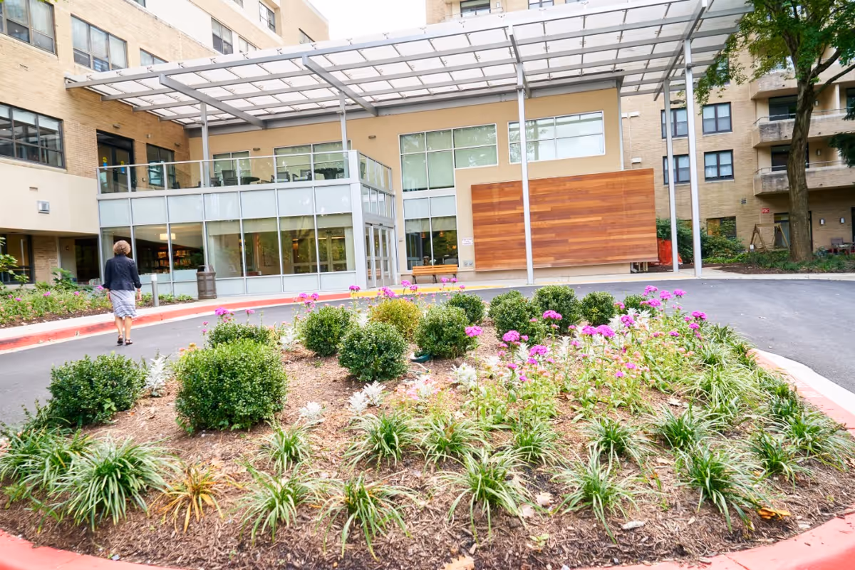 Exterior view of a senior living facility entrance with landscaped circular garden beds.