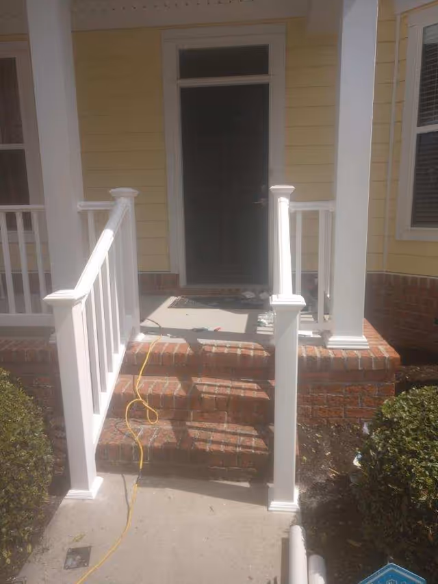 Yellow house entry with brick steps, white railing, and a dark front door.