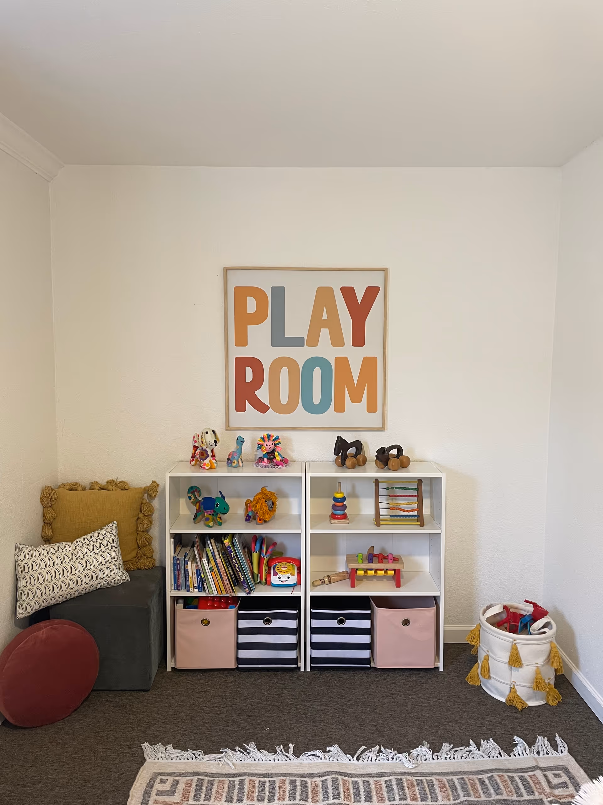 Small playroom with toy shelves, books, baskets, and a colorful 'PLAY ROOM' sign.