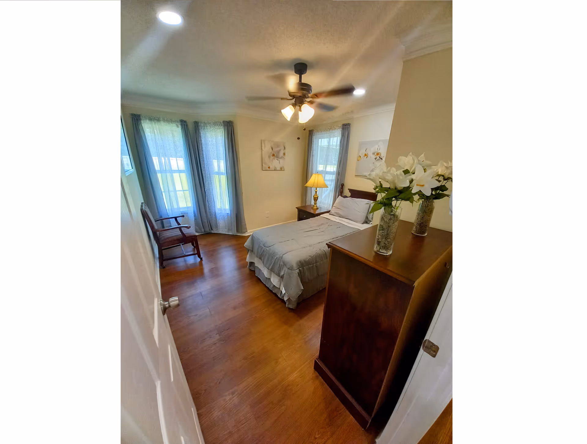 A cozy bedroom in Ridge Manor of Canton featuring a bed, dresser, lamp, and ceiling fan.