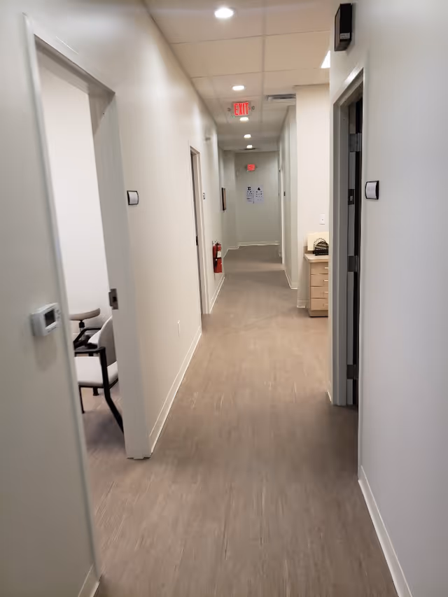 Bright hallway in a modern facility with doors, a desk, and exit sign at the end.