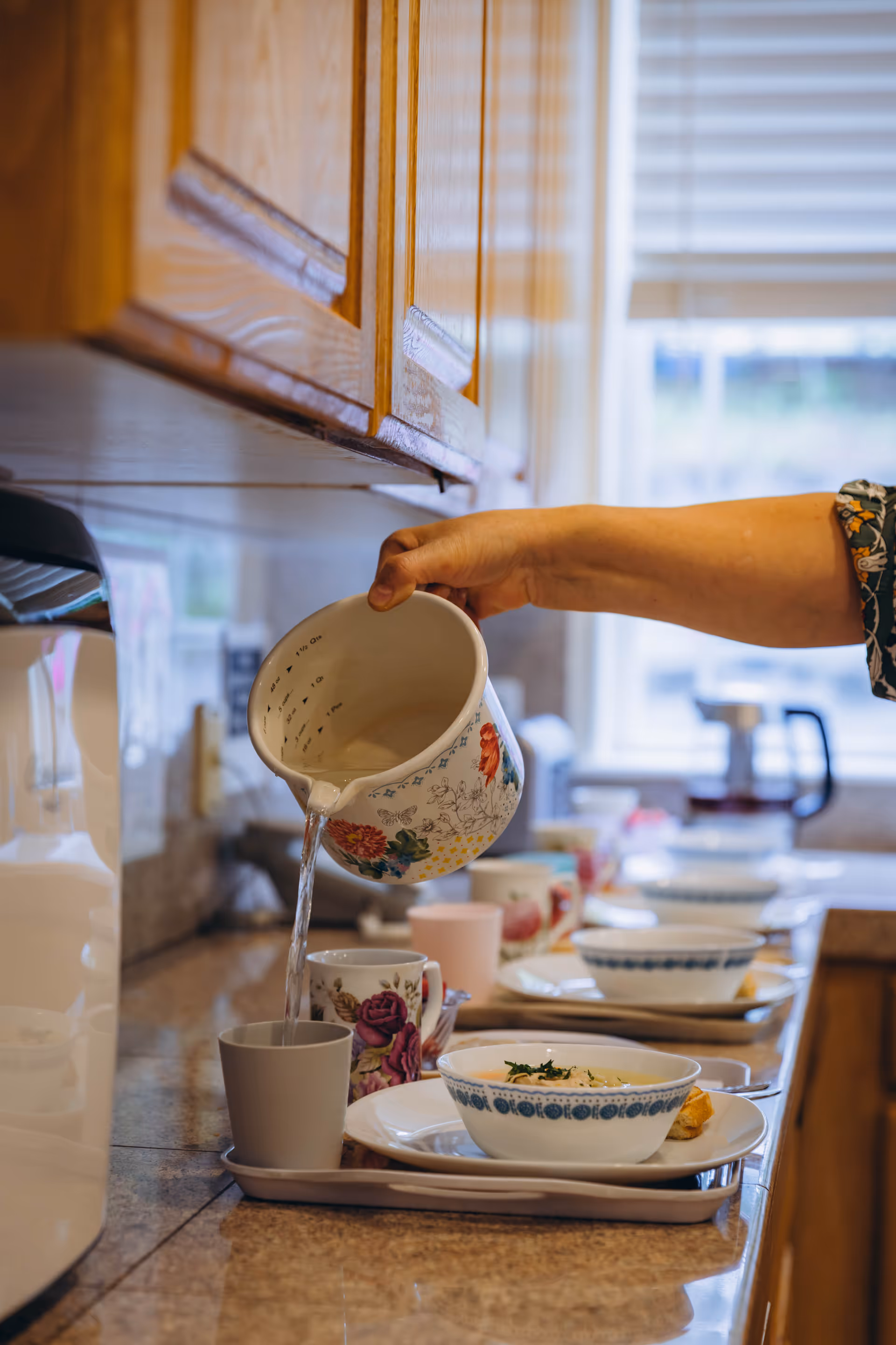 A hand pours water from a floral teapot into a mug on a kitchen counter.