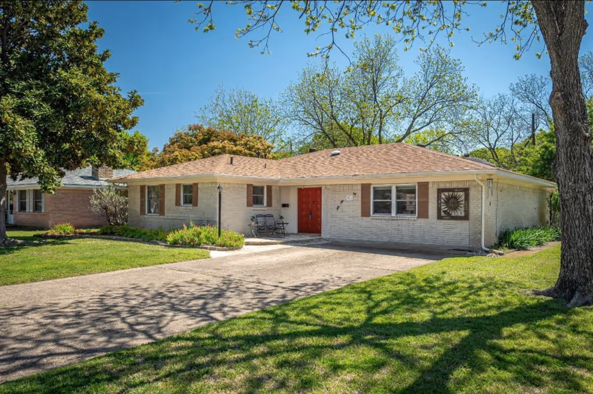 A single-story brick building with a red front door and surrounding trees on a sunny day.