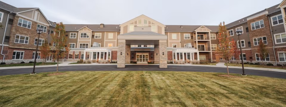 Front entrance of a multi-story senior living facility with a covered porte-cochère and a landscaped lawn in front.