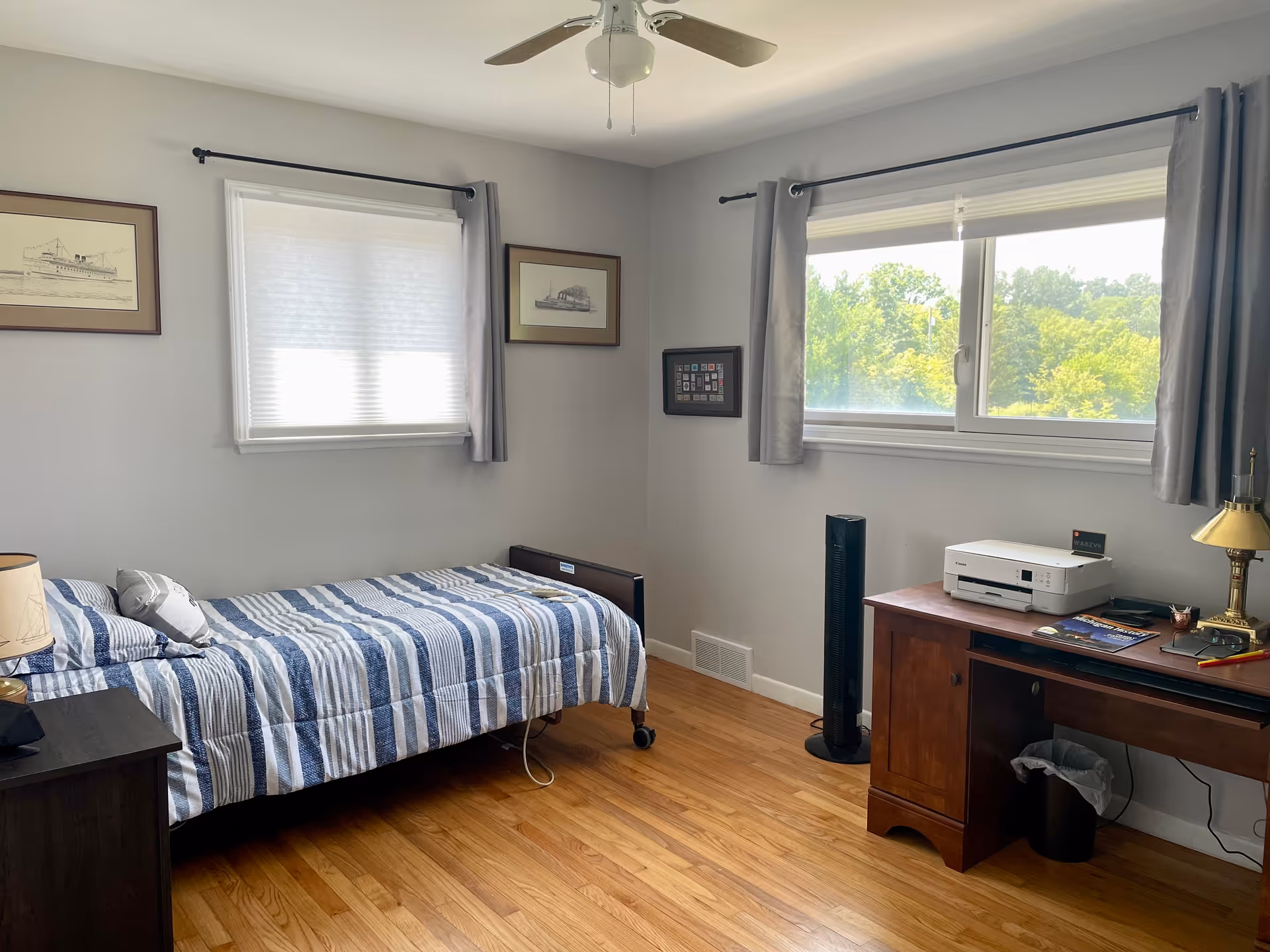 Small bedroom at Lyon's Trail Senior Living with a bed, desk, and windows.