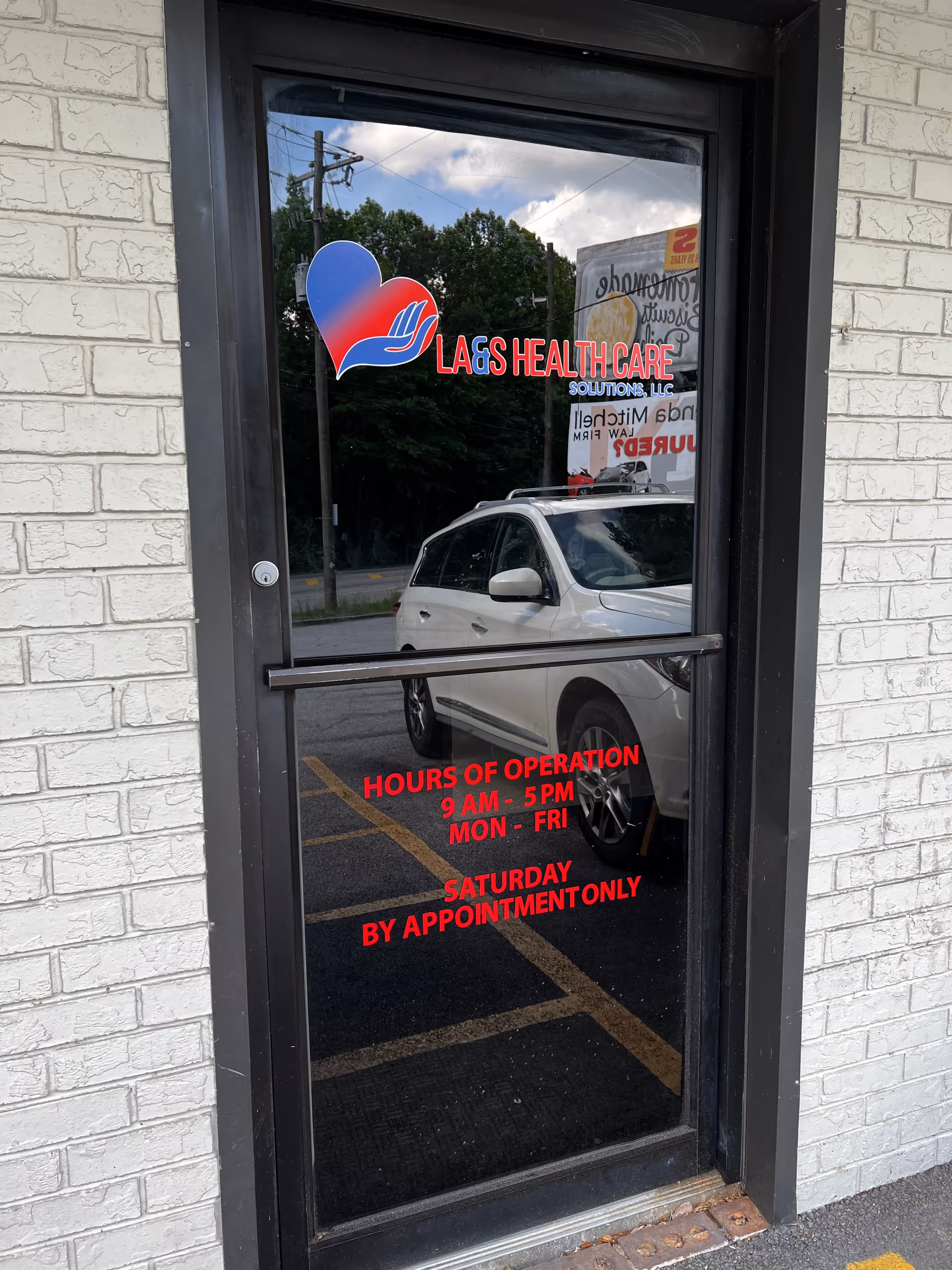 Glass front door with a heart logo and red hours text on brick exterior.