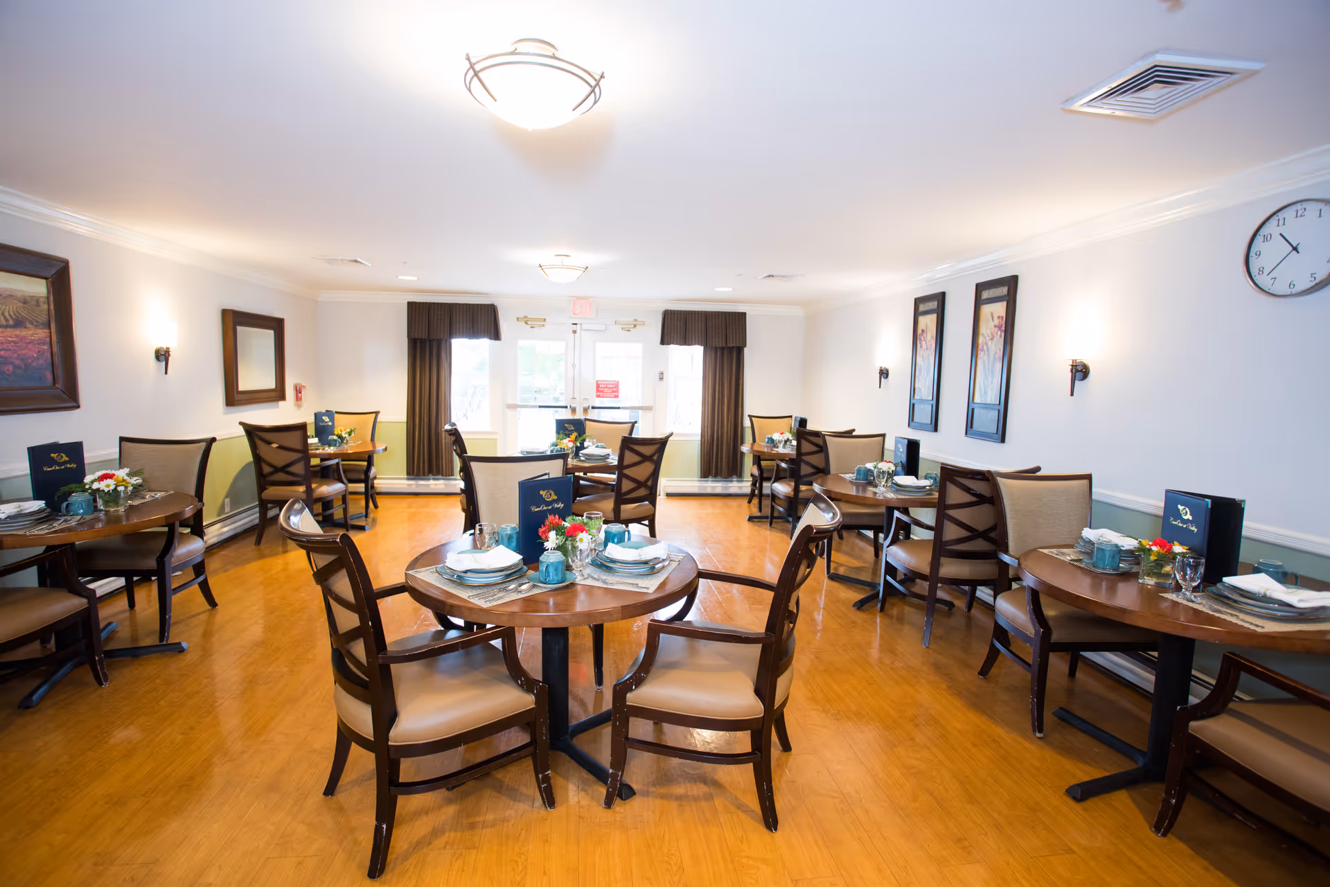 Bright dining room with round tables, chairs, and place settings in a senior facility.