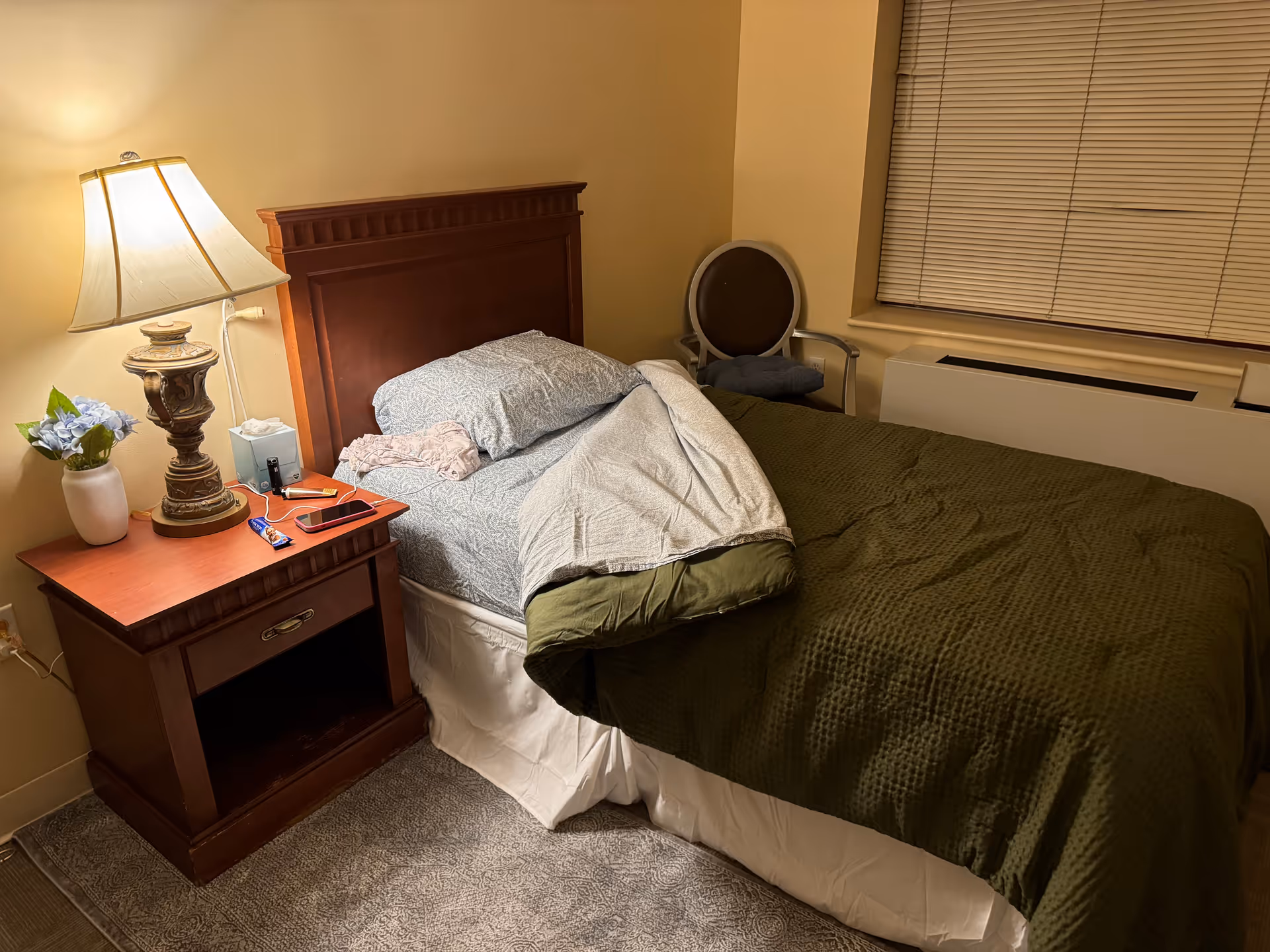 A bedroom with a wooden headboard bed, nightstand, lamp, and chair.