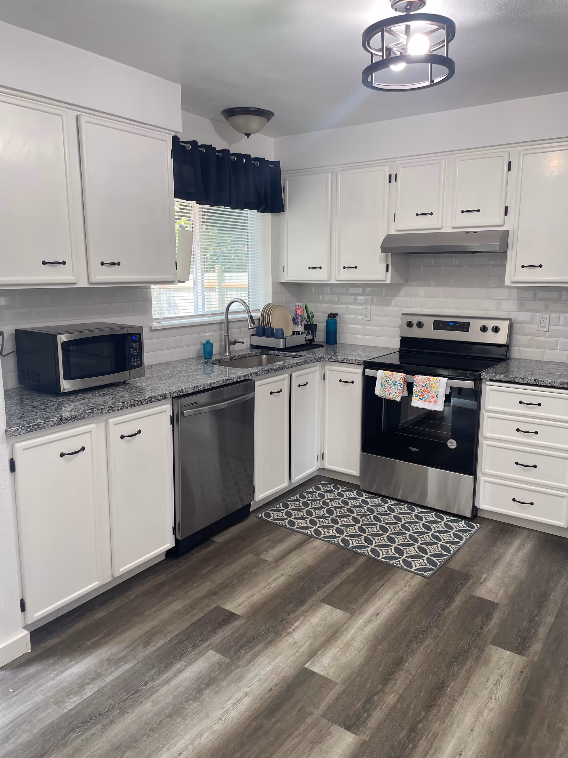 Bright white kitchen with stainless appliances, granite countertops, and a window over the sink.