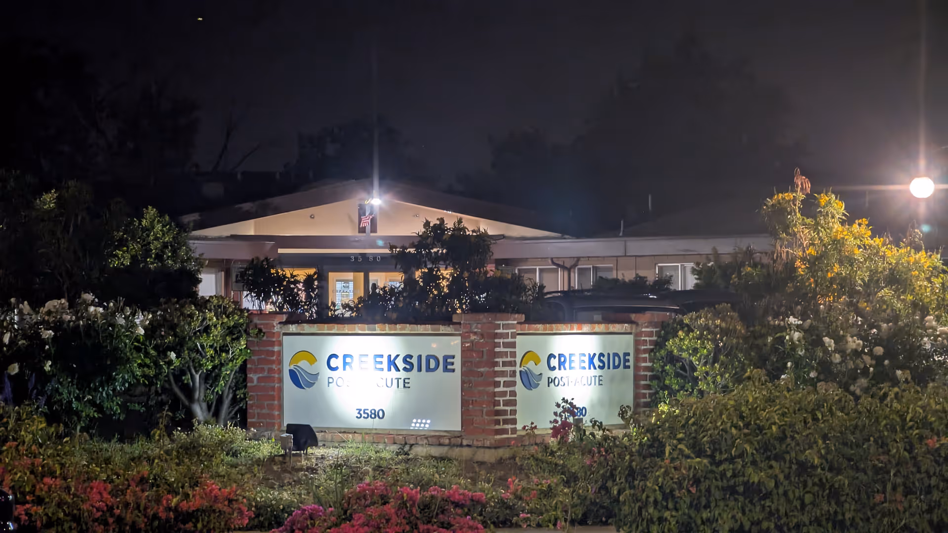 Nighttime exterior of a facility entrance with two illuminated Creekside Post-Acute signs.