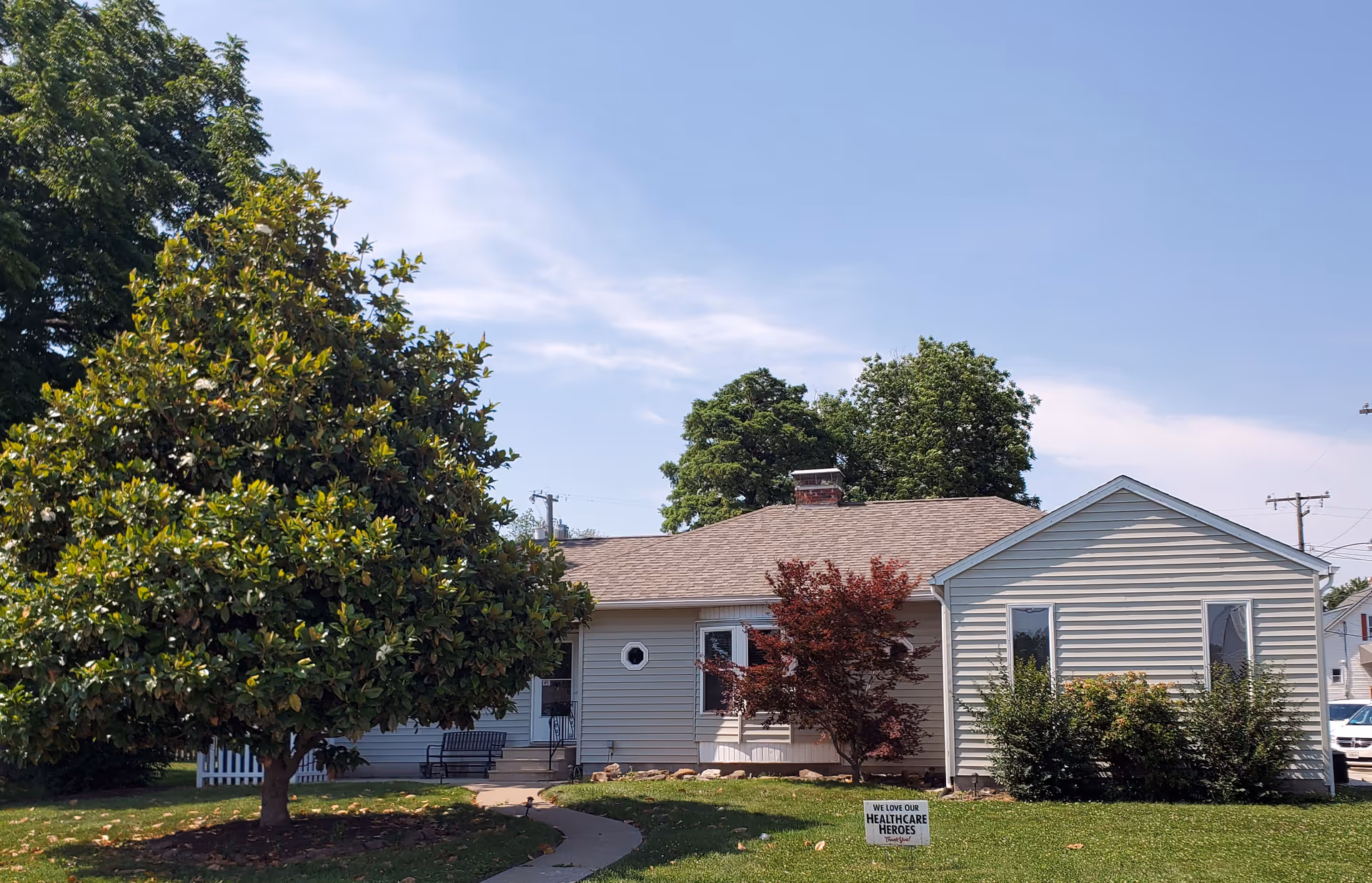 A single-story senior living facility exterior with a lawn, trees, and clear blue sky.