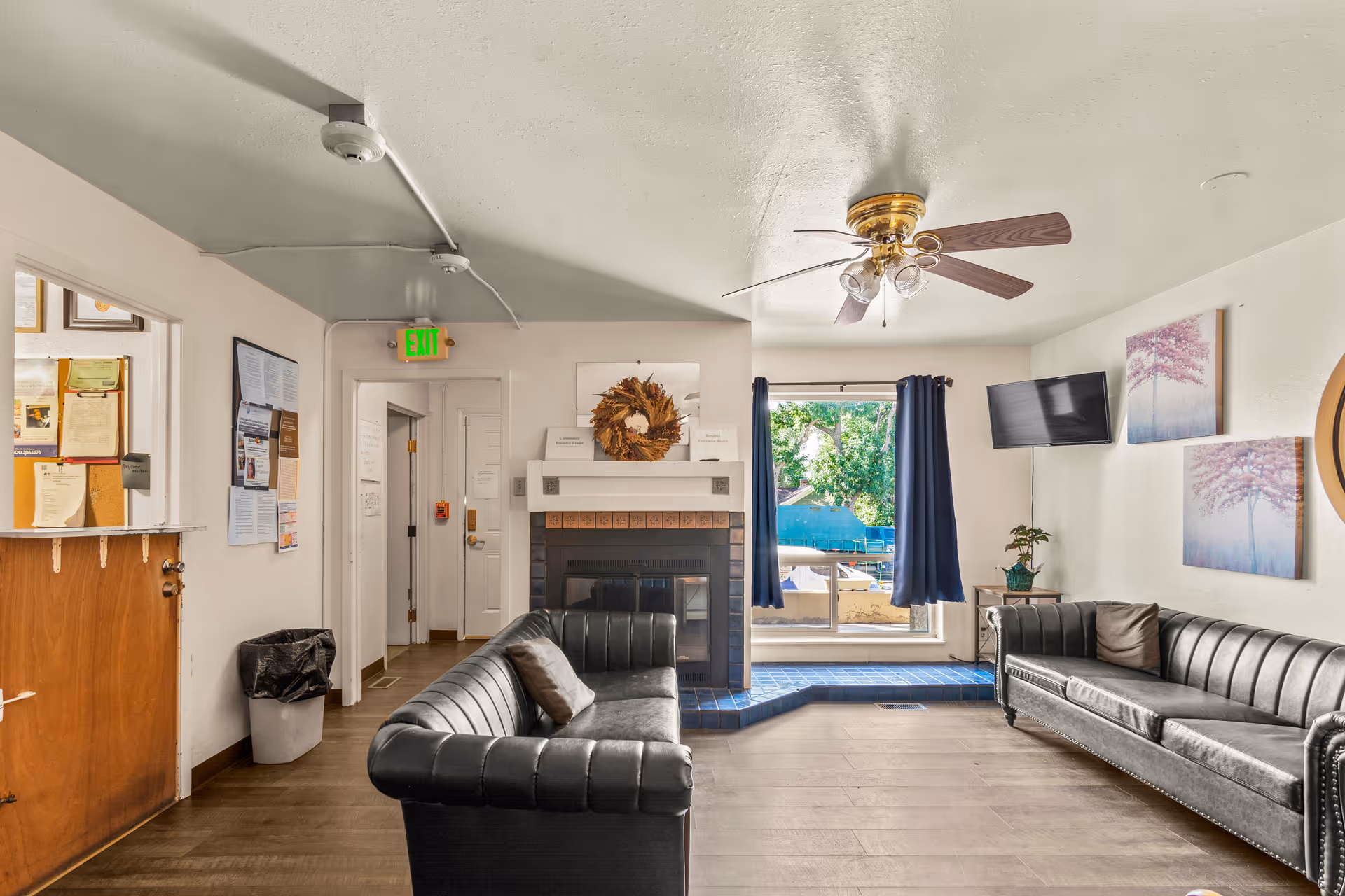 Cozy senior living lounge with leather sofas, fireplace, ceiling fan, TV, and patio access.