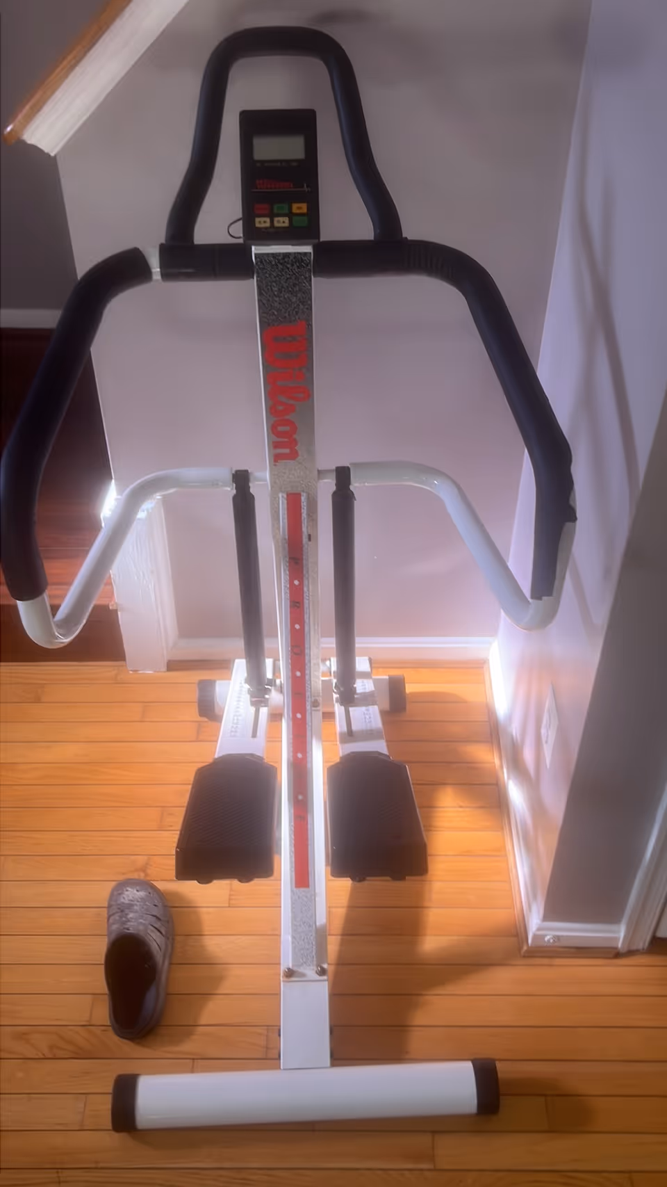 An indoor exercise machine with black handlebars, red vertical support, and a shoe on wooden floor.