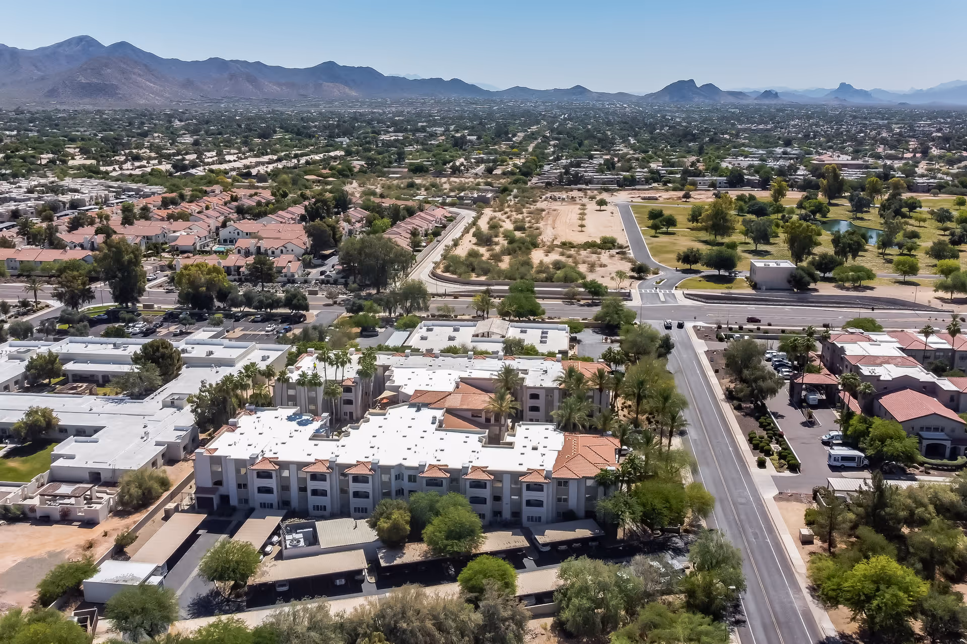 Aerial view of a senior living complex with white roofs amid desert and mountains.
