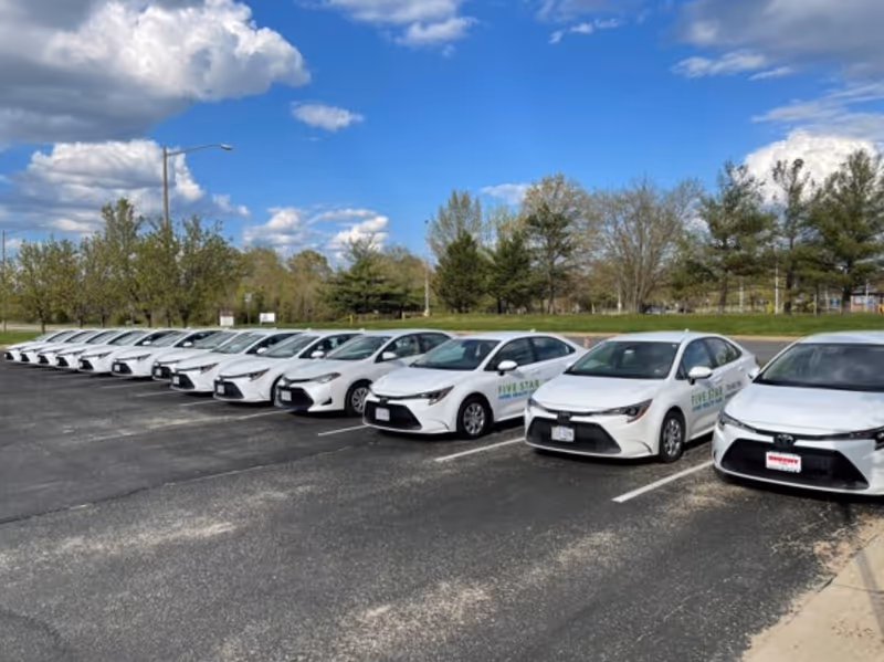 Row of white company cars parked in a lot beneath a blue sky.
