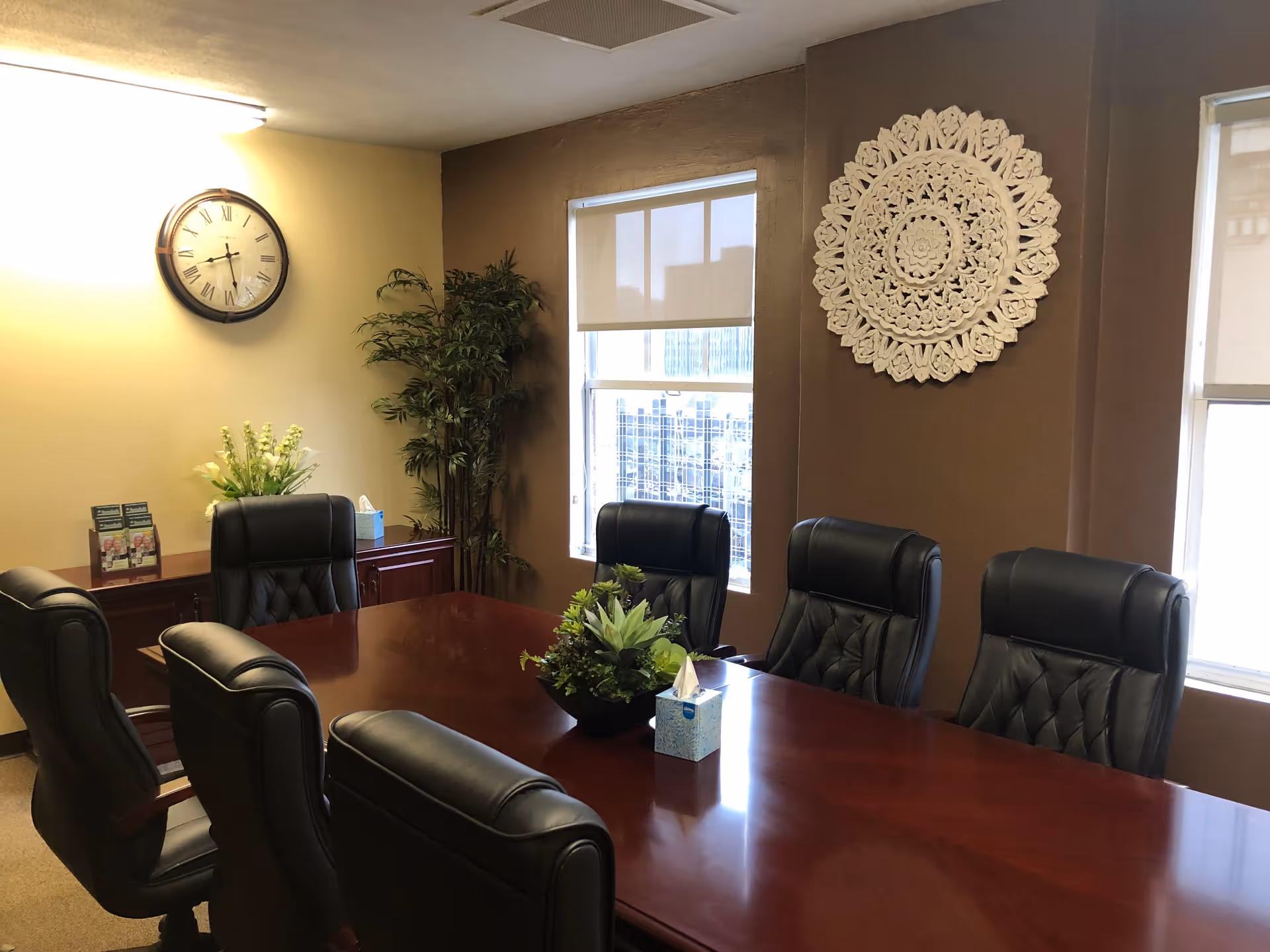 A polished conference table with leather chairs, plants, clock, and decorative wall art.