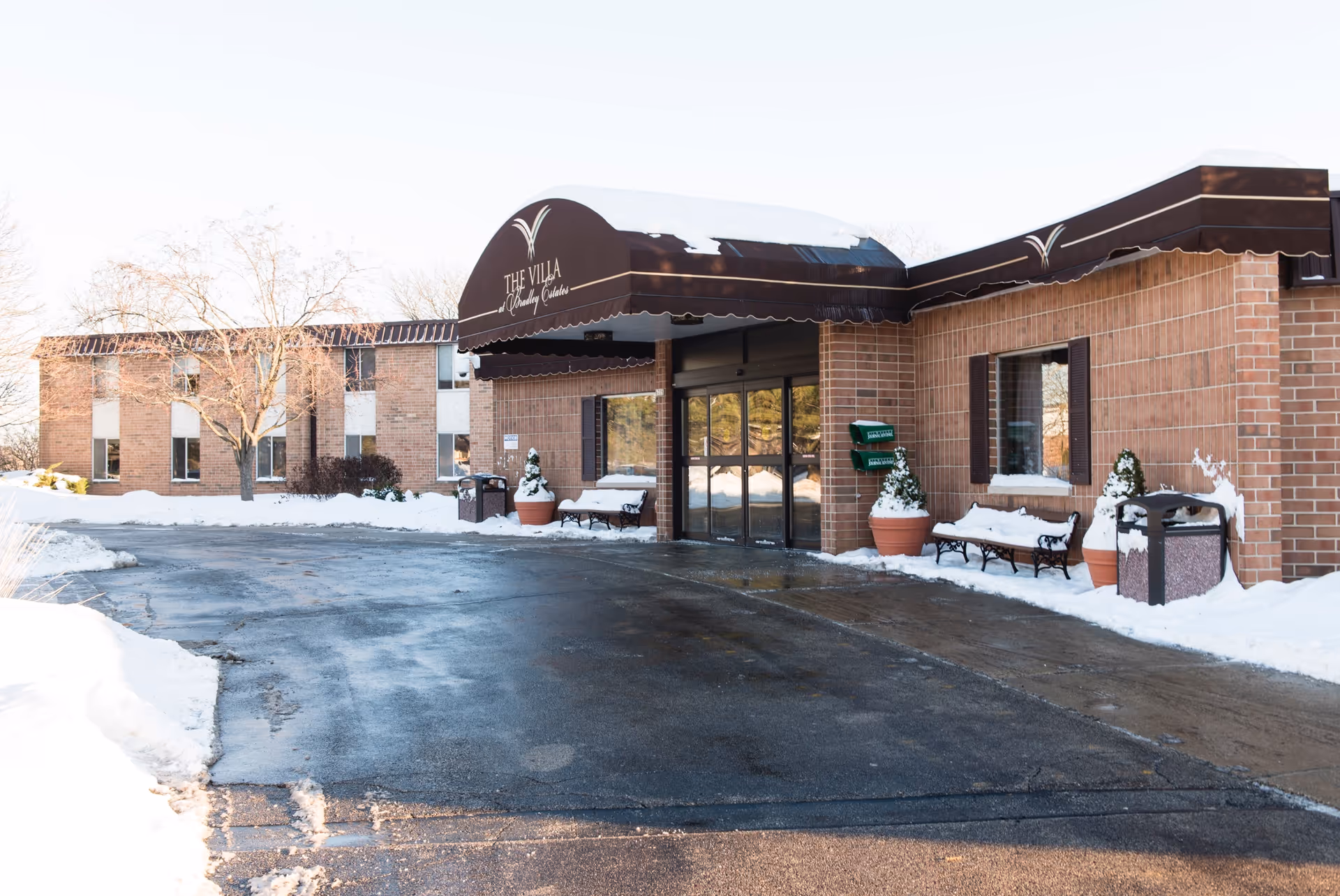 Exterior view of Villa at Bradley Estates entrance with snow, brick building, and benches.