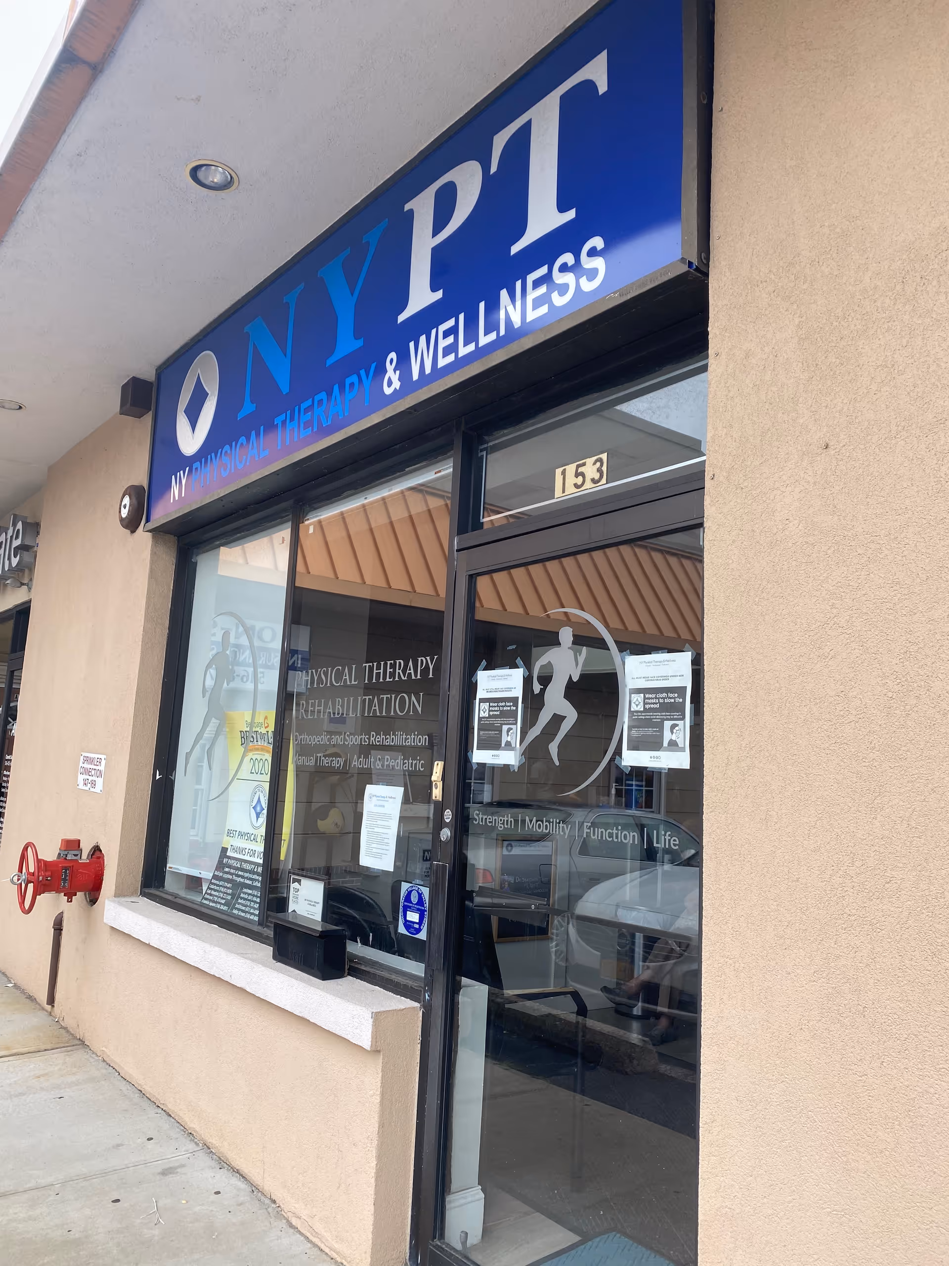 Exterior view of a physical therapy clinic storefront with blue NYPT sign and glass doors.
