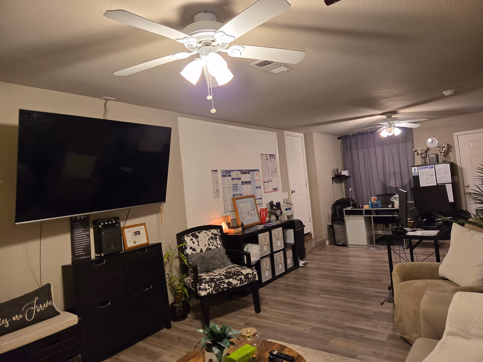 Living room in a senior facility with large TV, sofa, desk, and chairs.