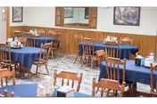 A dining room with blue tablecloths, wooden chairs, and framed wall art.